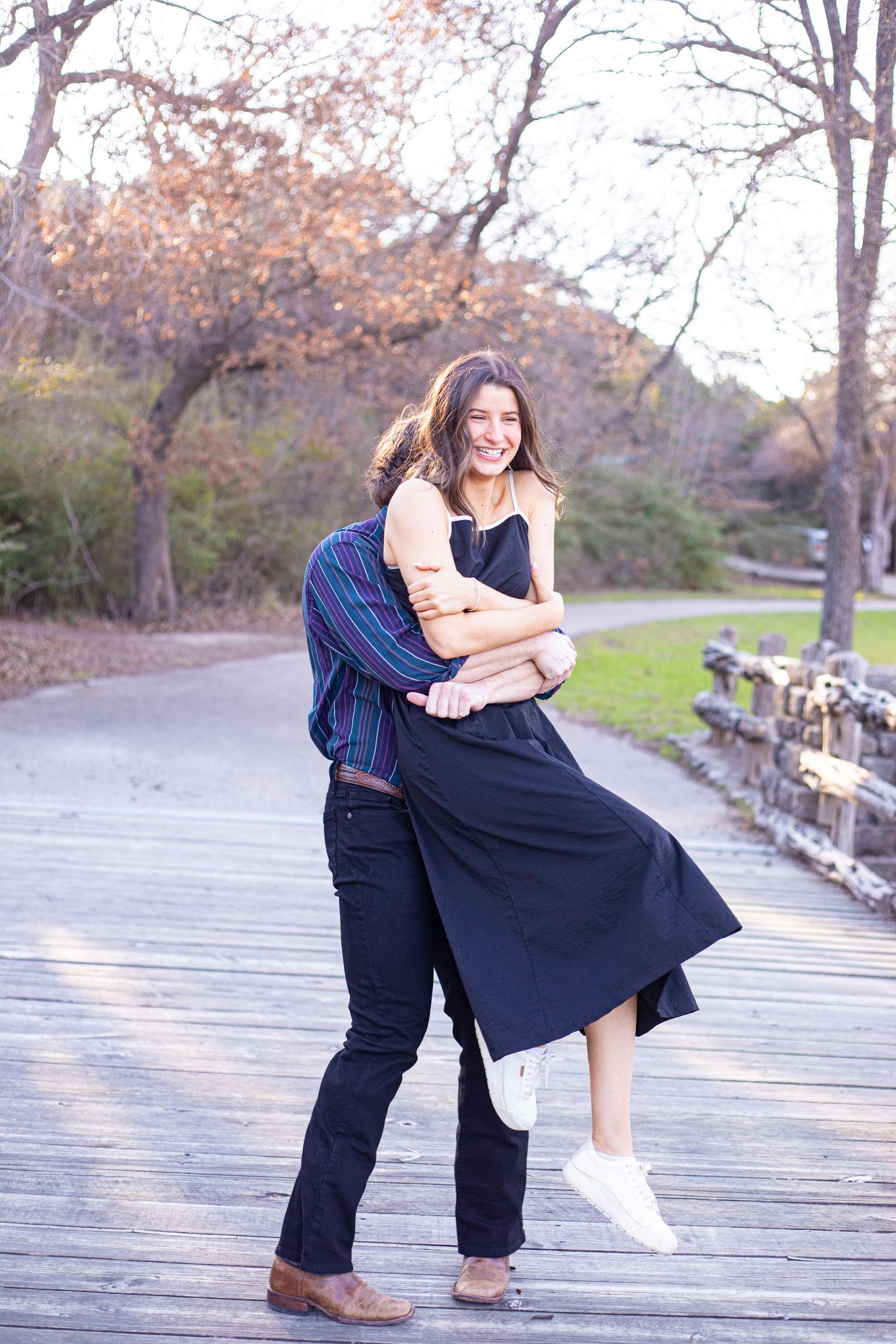 Couple dancing and twirling on wooden boardwalk surrounded by autumn trees.