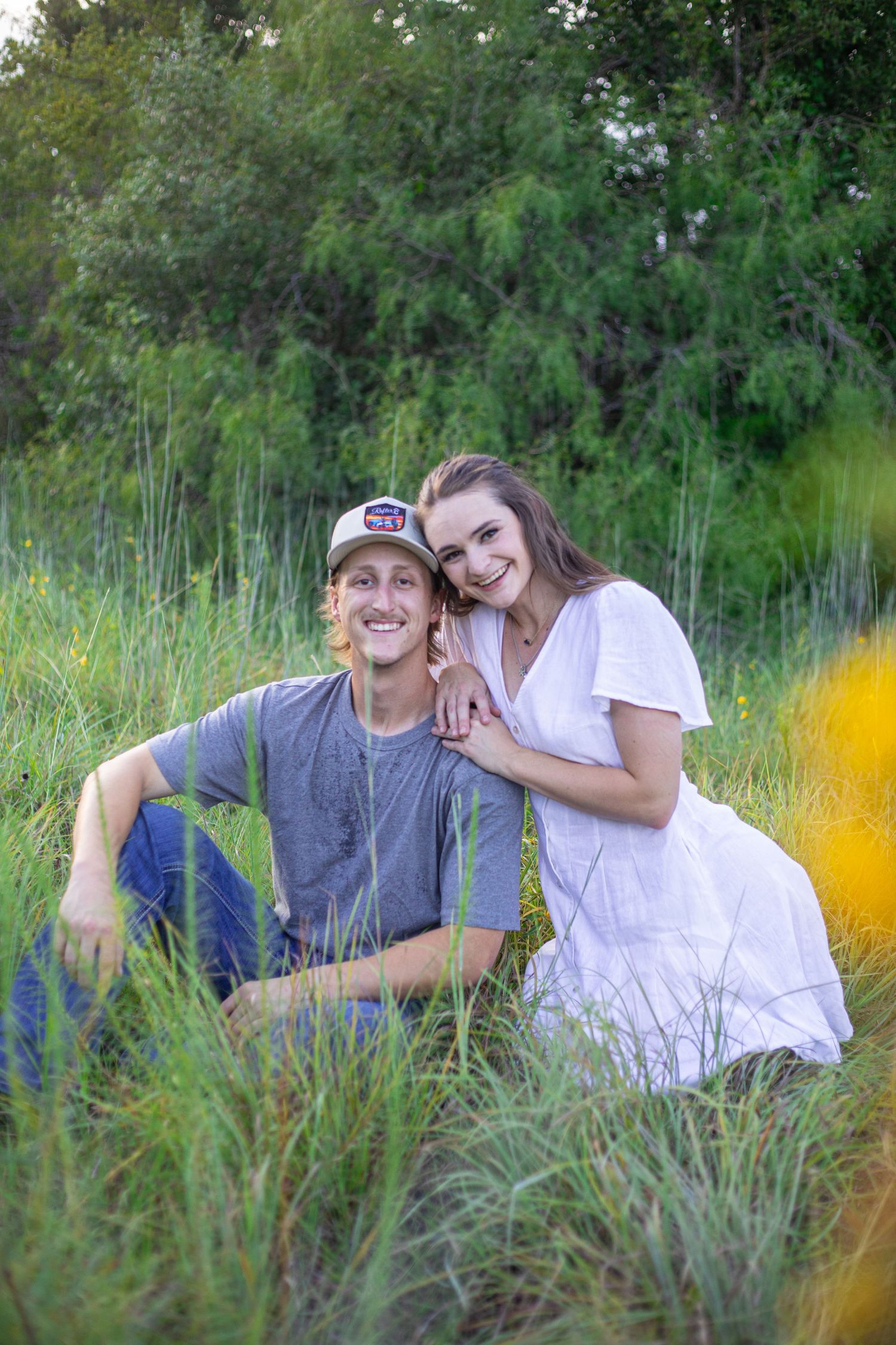 A couple lies together in tall grass during a romantic outdoor photoshoot.
