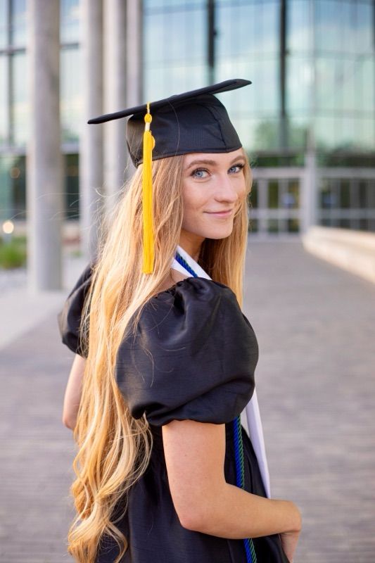 Graduate in black cap and gown posing in front of modern architectural columns.