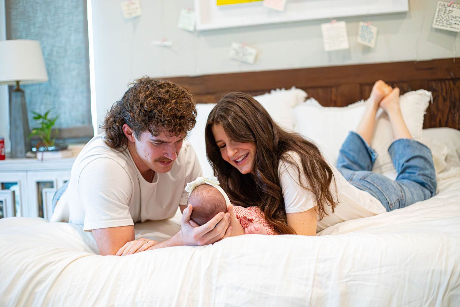 Happy couple lying on bed admiring their newborn baby in a cozy bedroom setting.