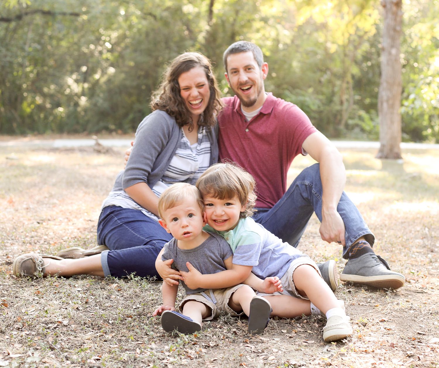 Playful family photo session with everyone sitting together on the ground outdoors.