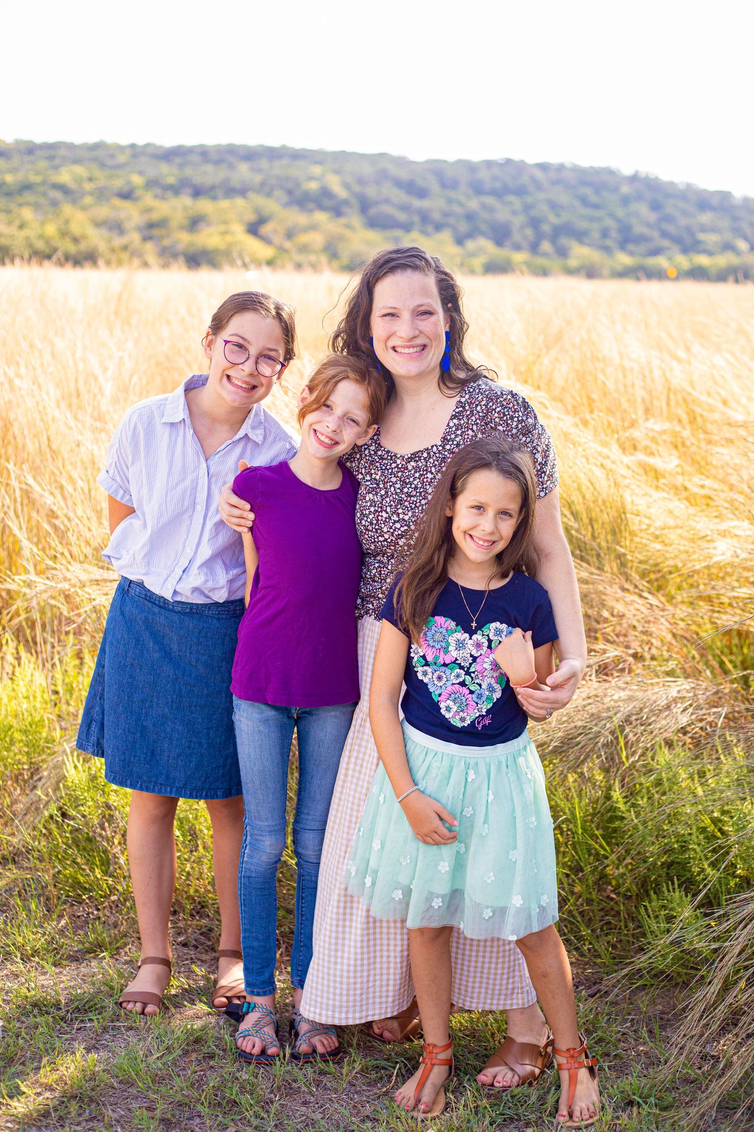 Children posing together in field during sunset with tall grass and rolling hills in background.
