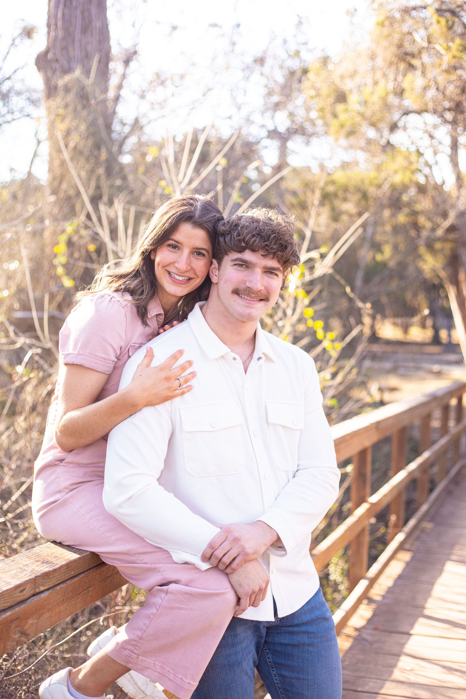 A couple sits close together on a wooden boardwalk surrounded by autumn foliage.