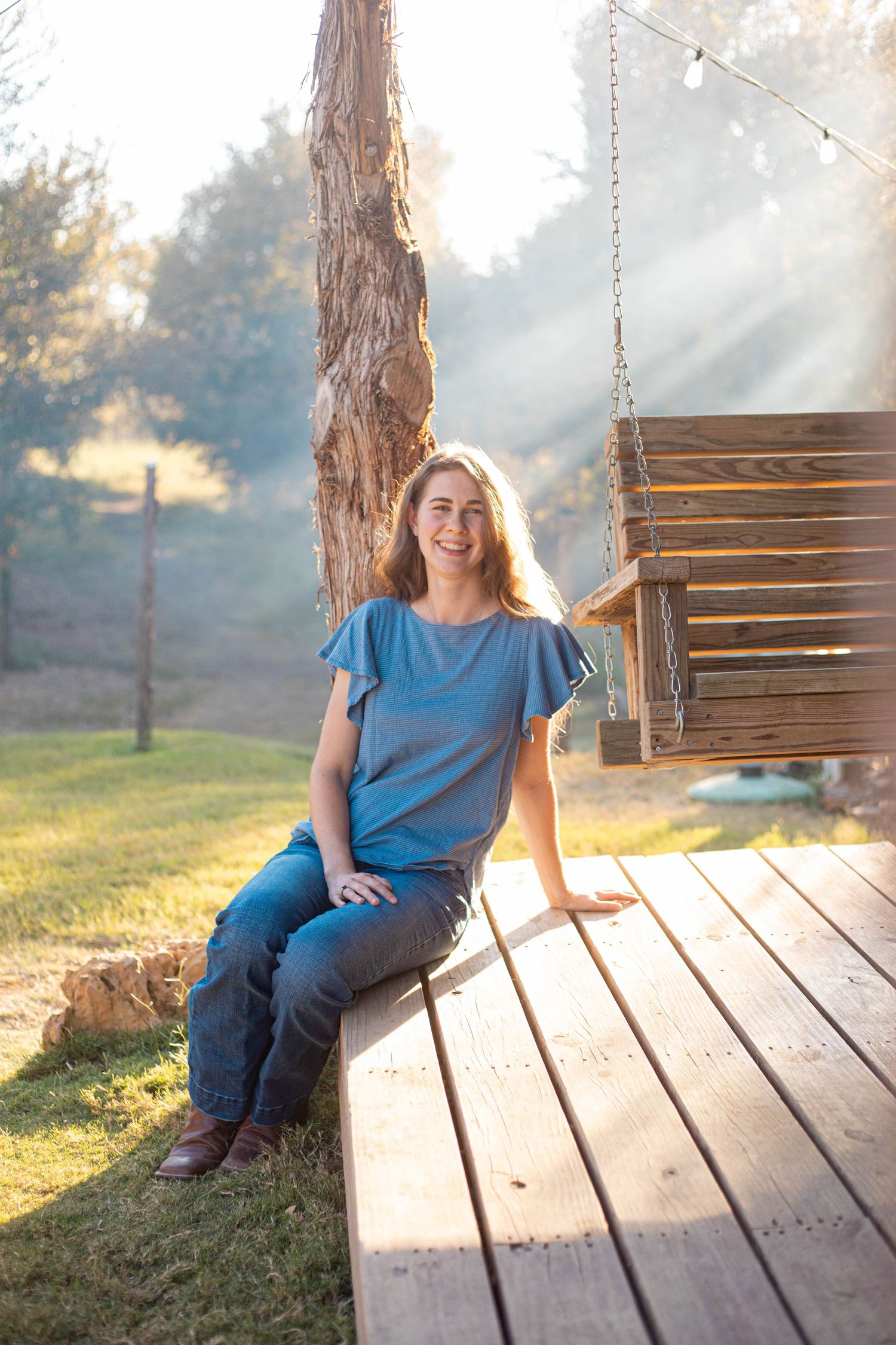 Person in blue shirt sitting on wooden deck swing during golden hour sunset.