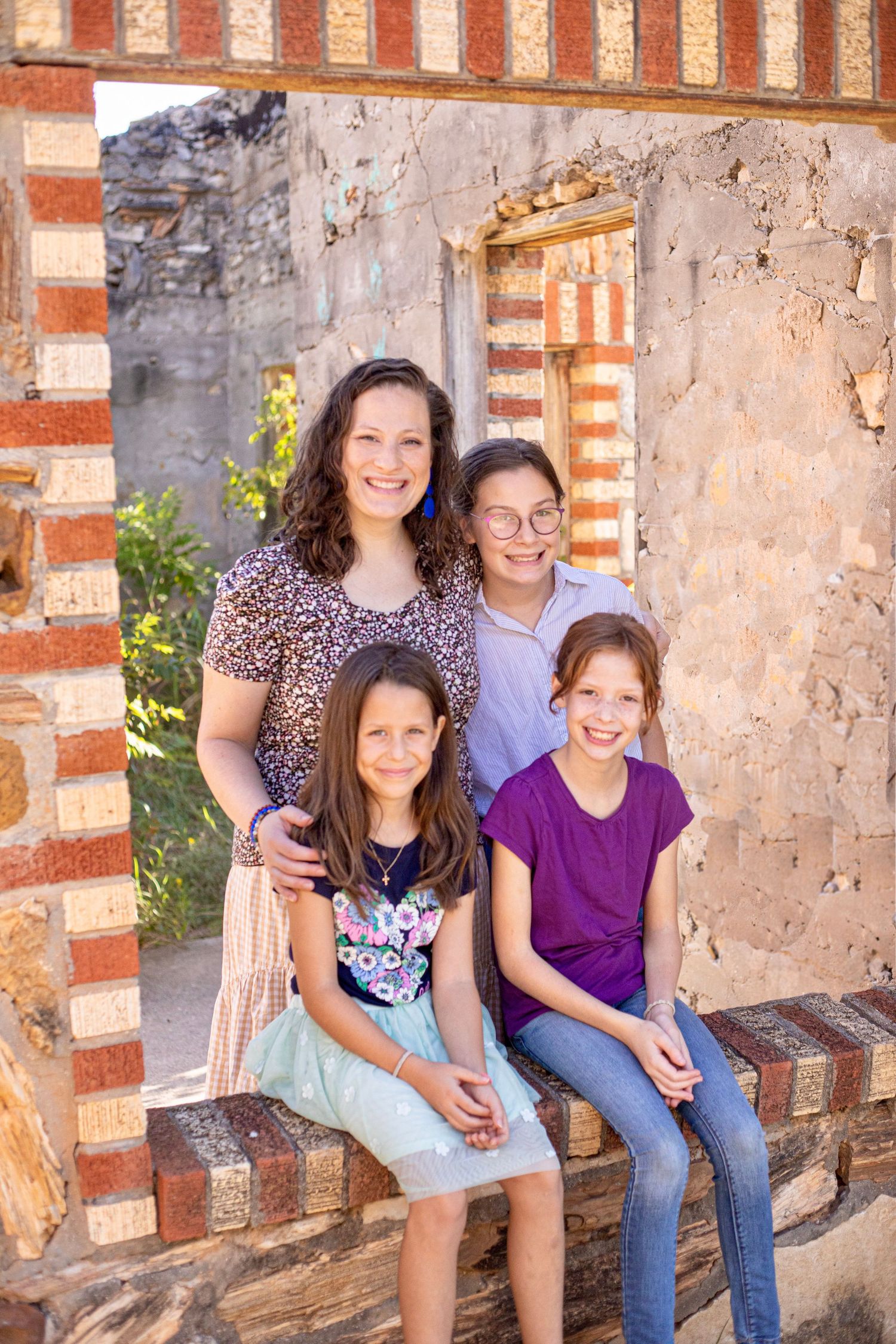 Family portrait with four people sitting together on brick steps against stone wall with red accents.