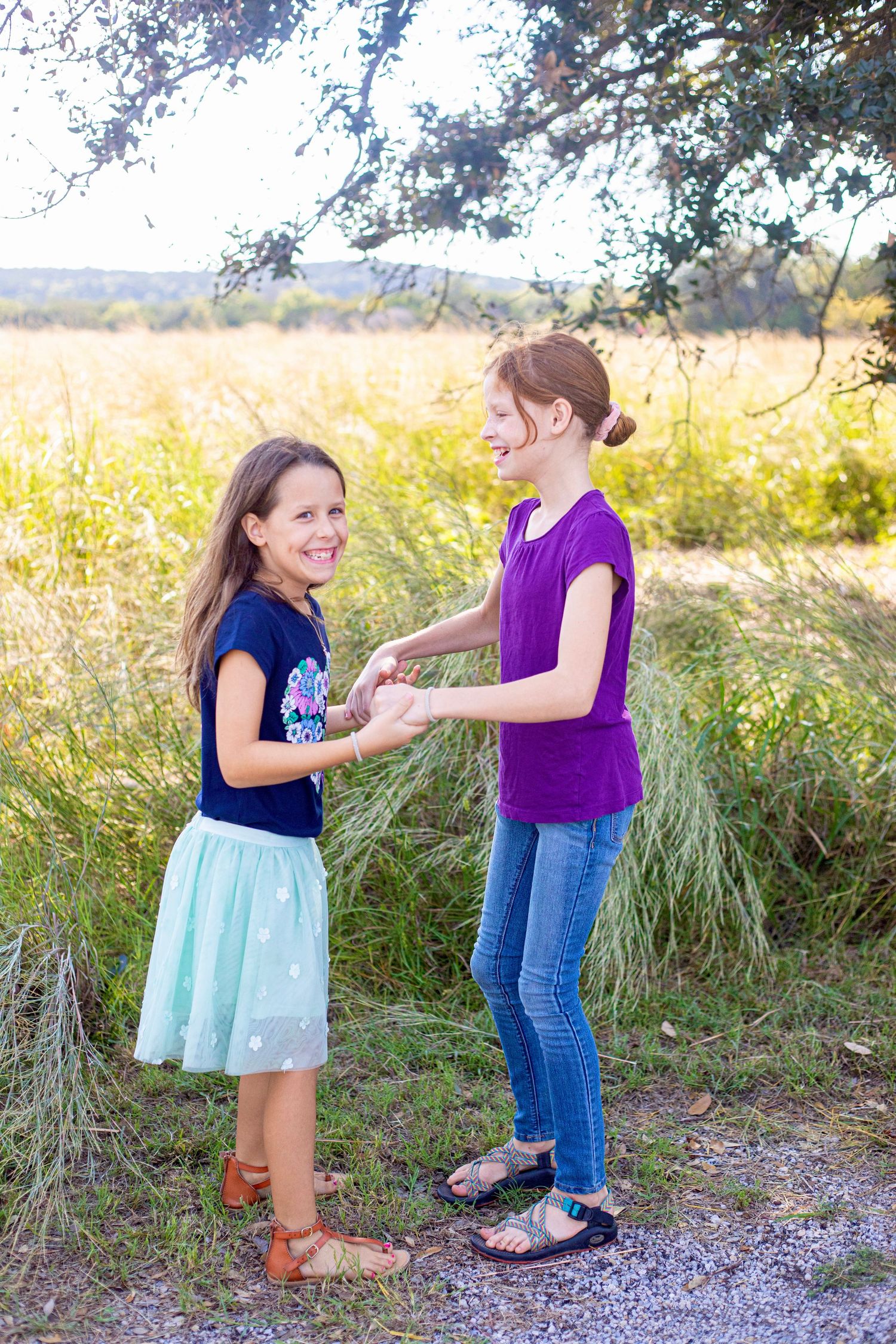 Children playing together on a gravel path surrounded by tall grass and trees.