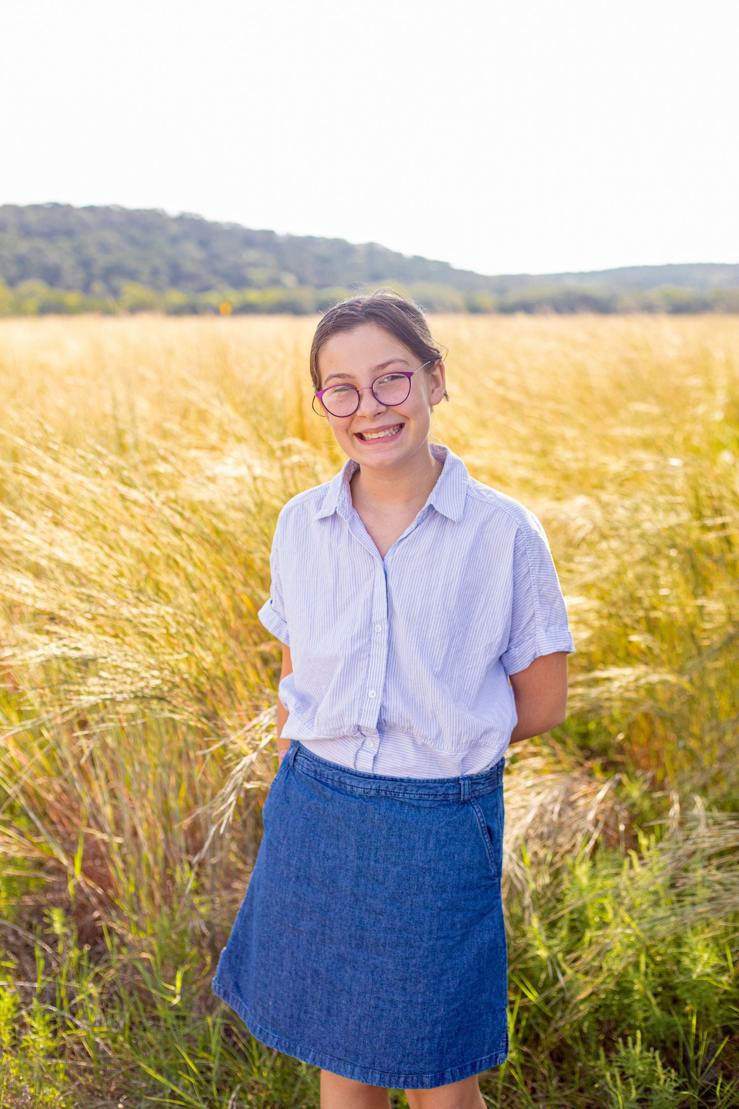 A person in a light blue shirt and denim skirt poses in a golden wheat field.