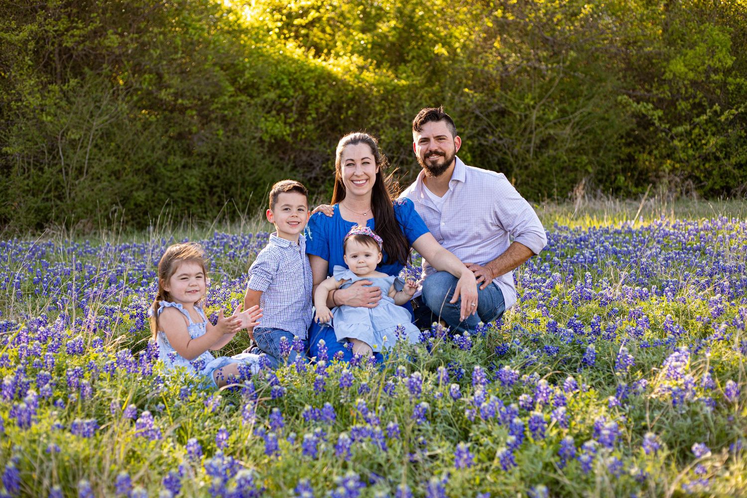 Family of five posing in a field of blooming bluebonnets during golden hour in Texas.