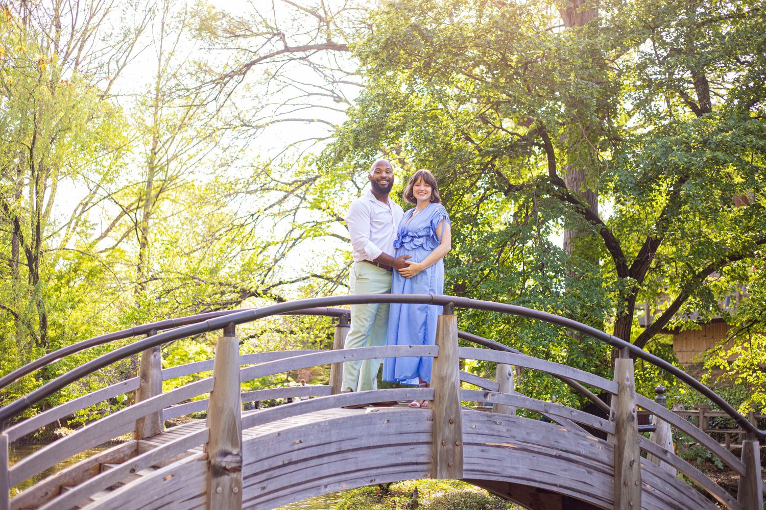 Couple relaxing on wooden bridge in lush garden setting during sunset.