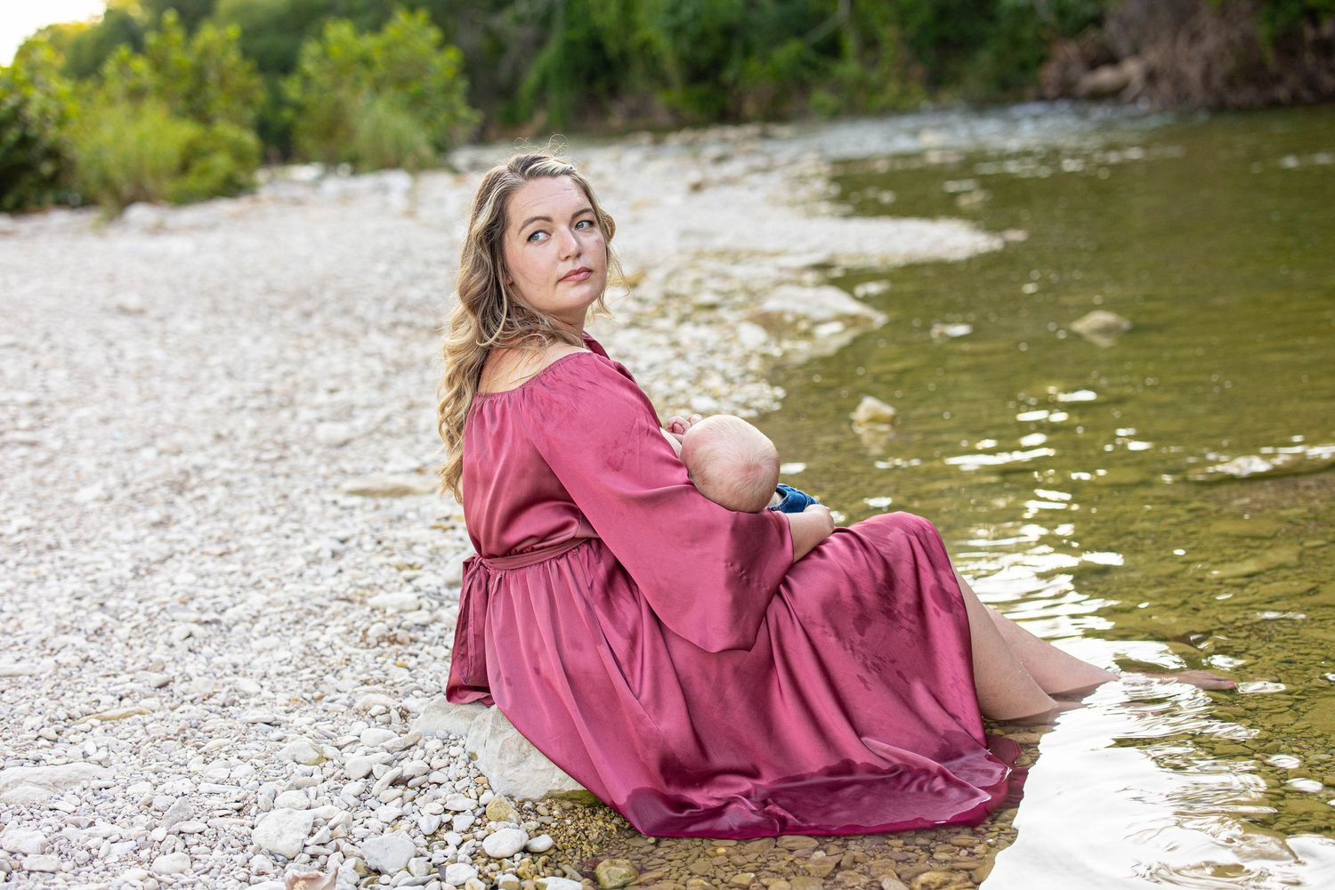 A serene portrait by the water featuring a flowing pink dress against a rocky shoreline.