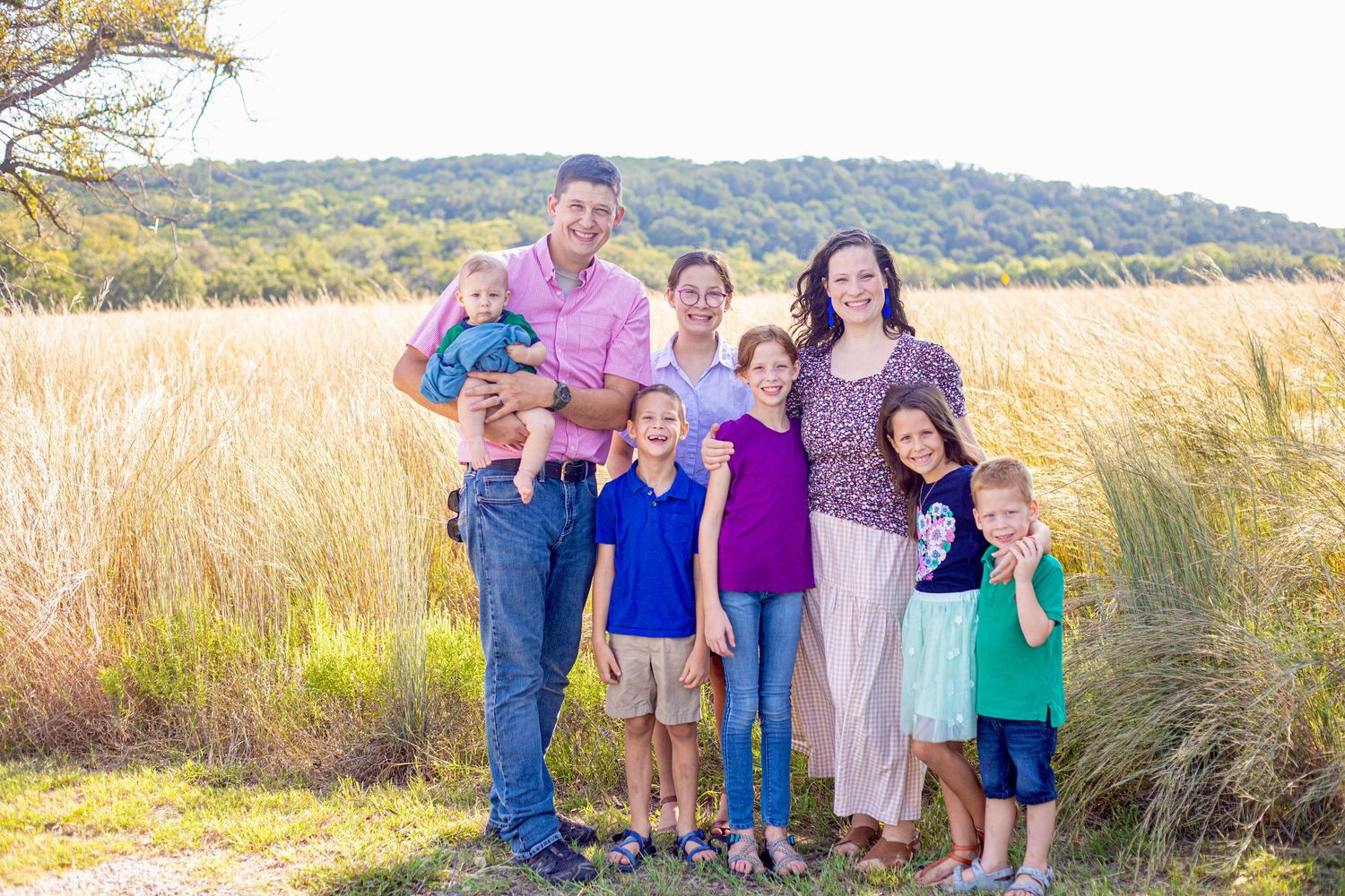 Family portrait in a natural setting with mountains and golden grass in the background.