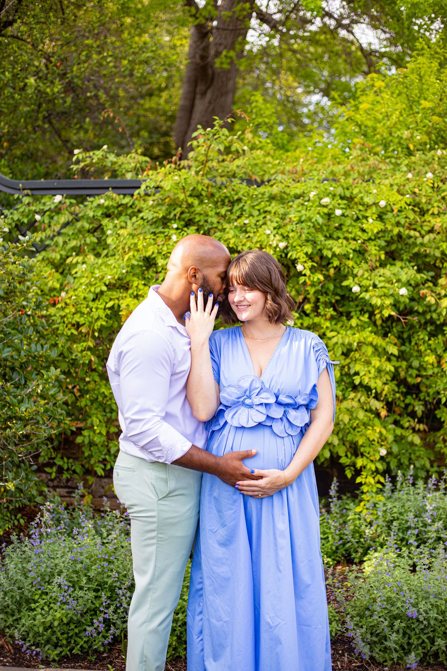 A tender maternity moment captured in a garden with lush greenery and flowering plants.