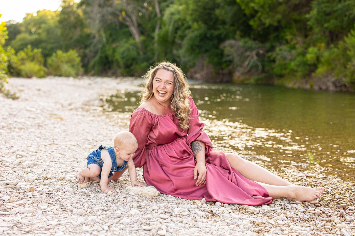 A couple poses together on a rocky riverbank during a summer photoshoot.