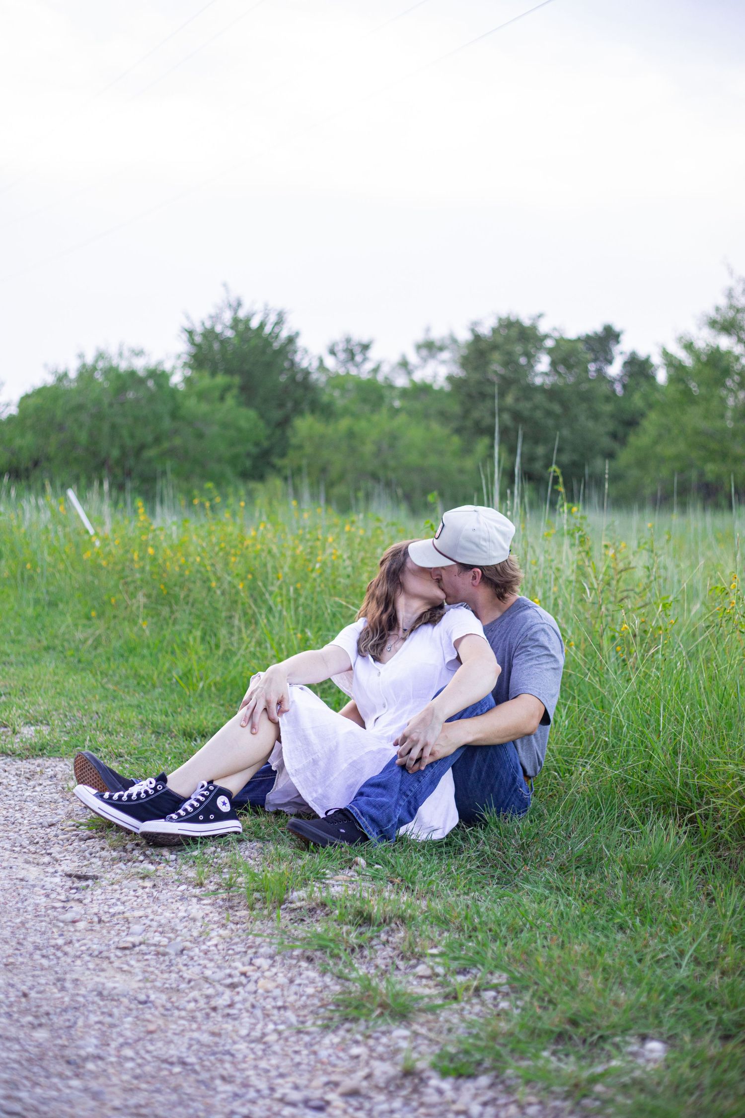 A couple relaxes together on a gravel path next to a grassy field.