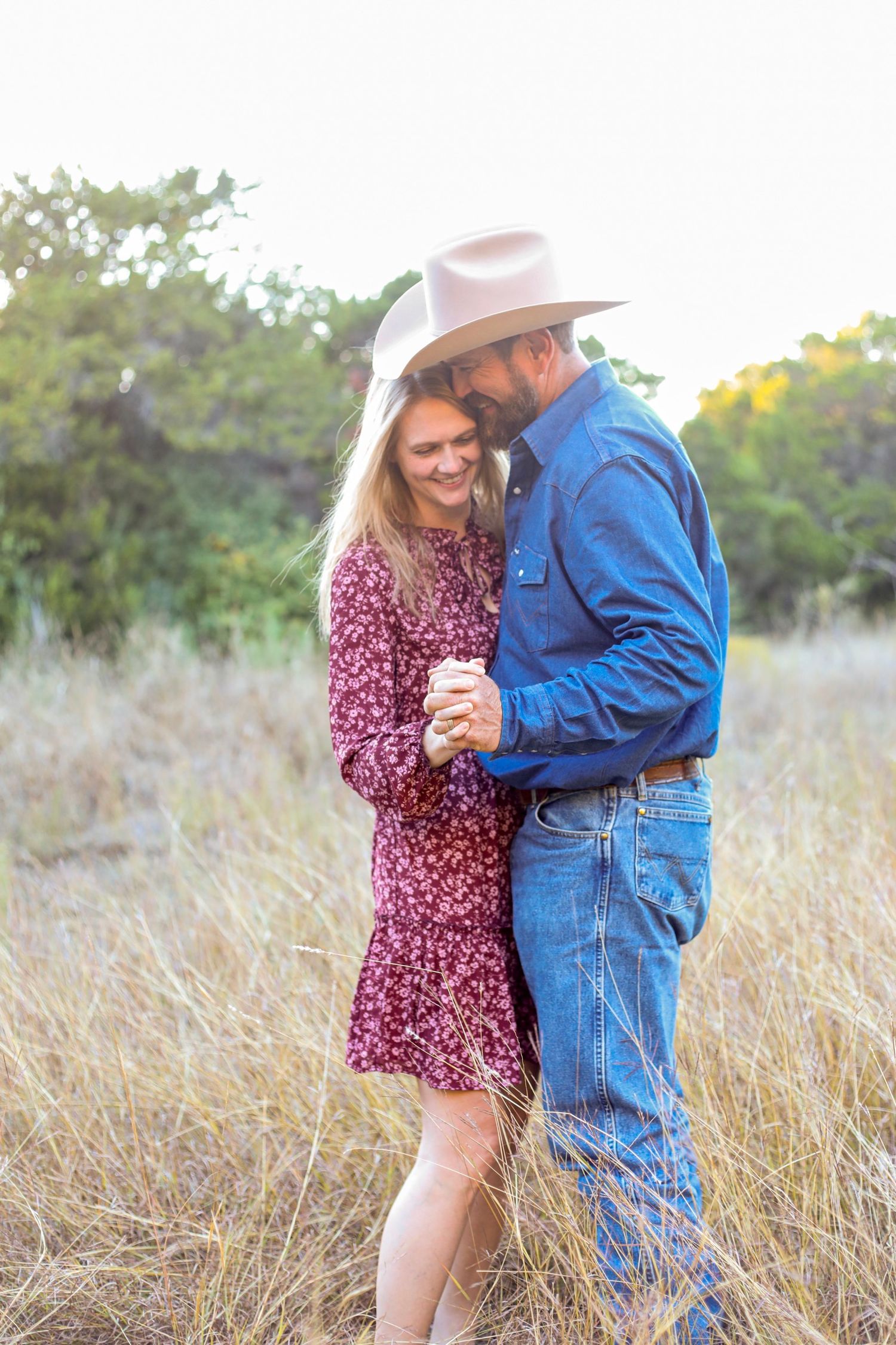Couple in western wear shares intimate dance in rustic field setting.