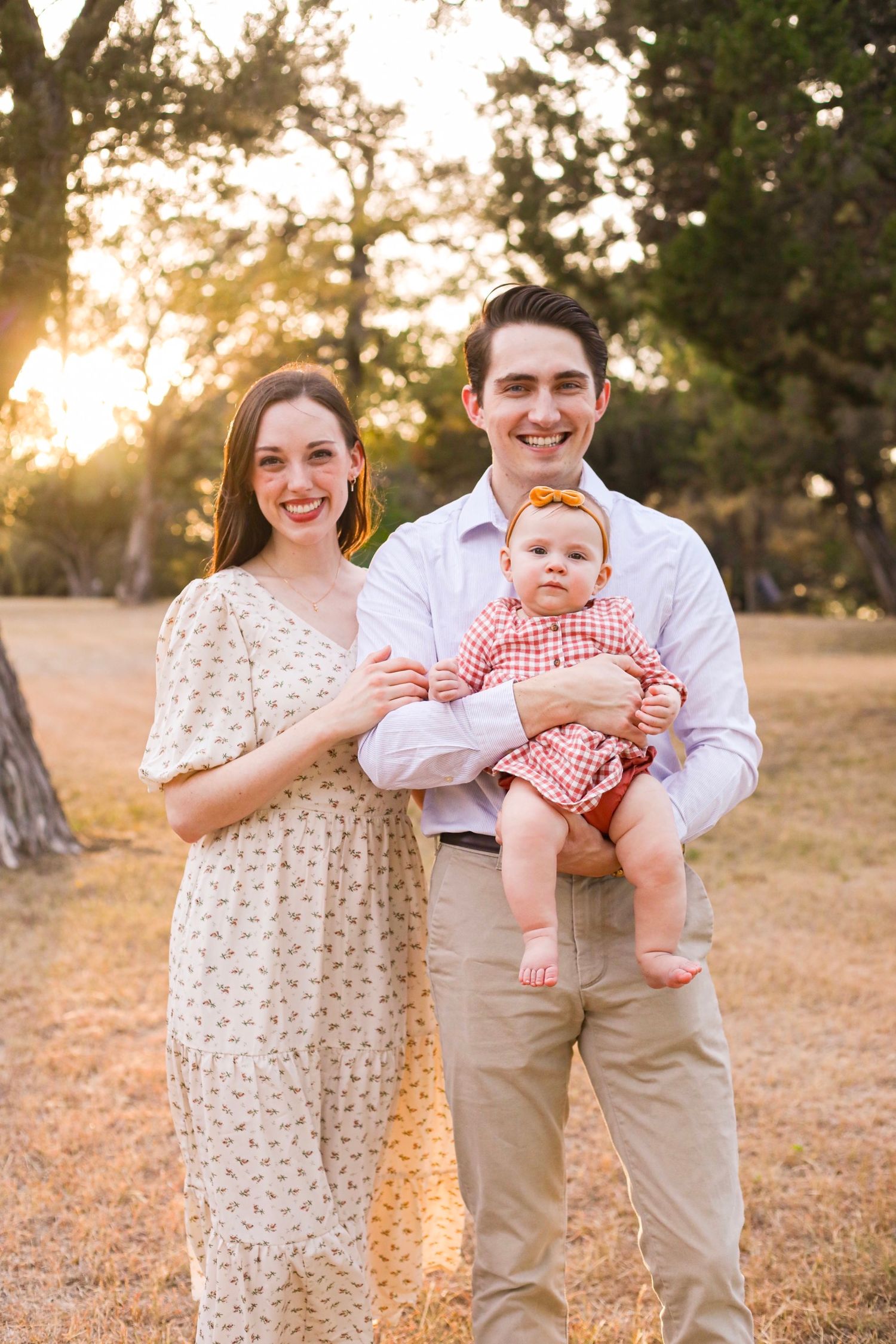 A couple with an infant pose together in a natural outdoor setting during golden hour.
