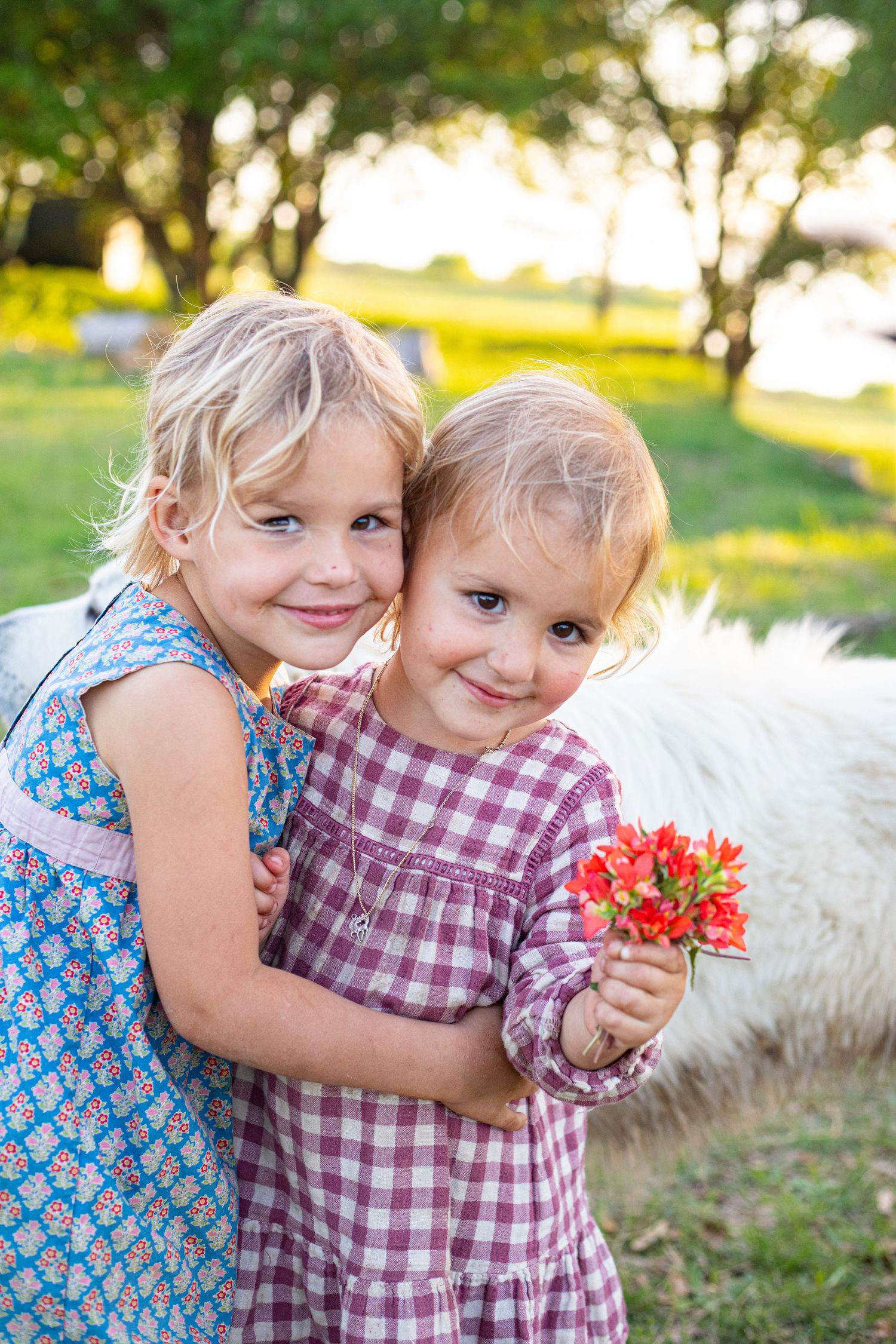 Two children hold flowers while posing together outdoors.