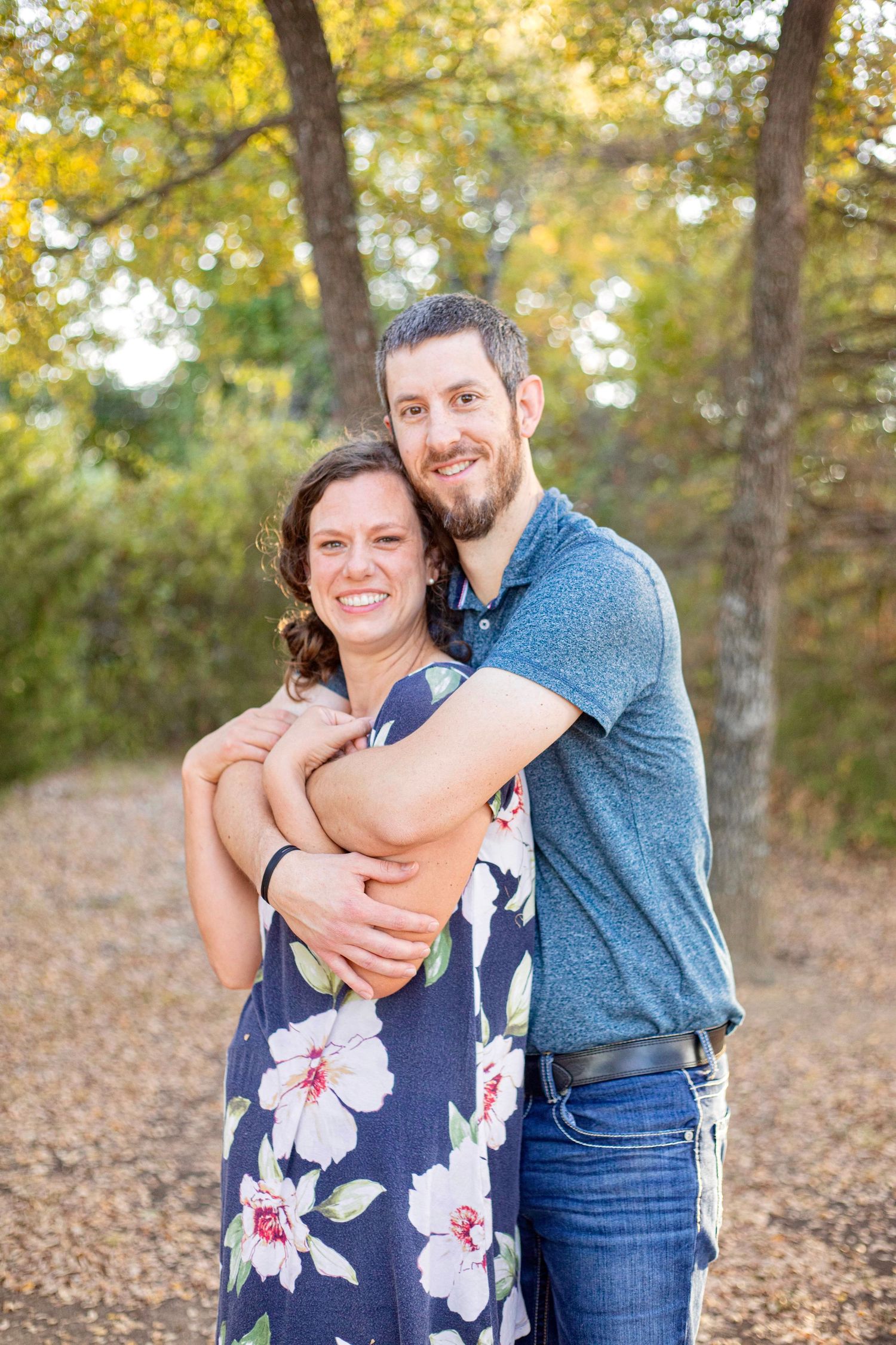 Couple embracing in a sunlit autumn forest wearing casual attire.