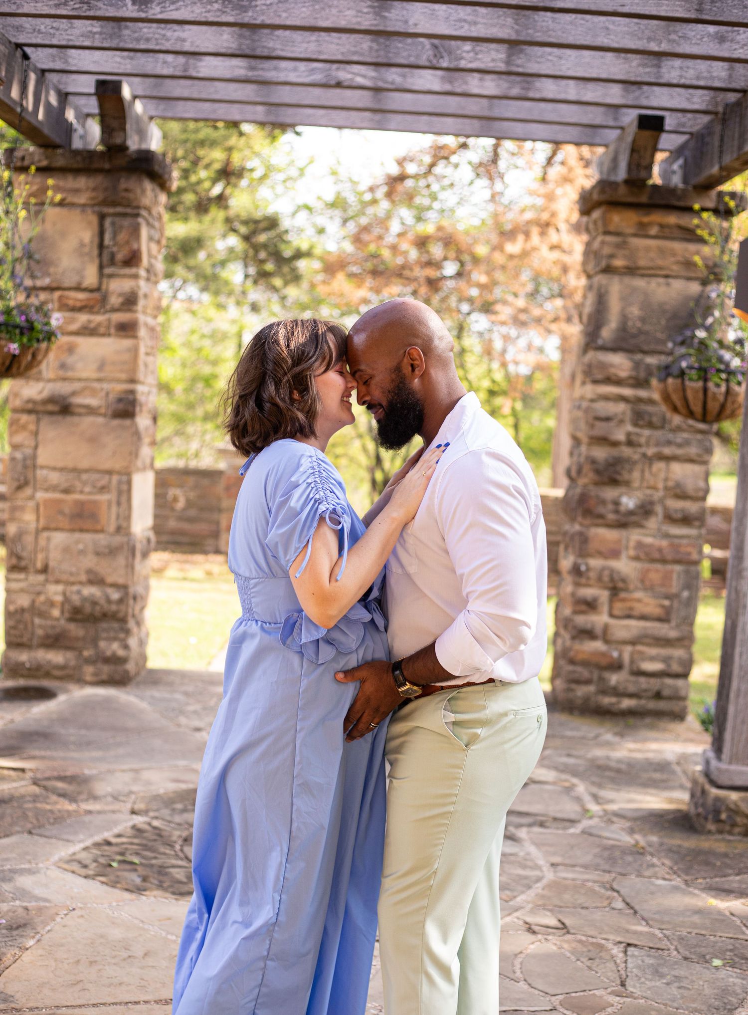 A tender embrace between a couple under a rustic wooden pergola with stone columns.