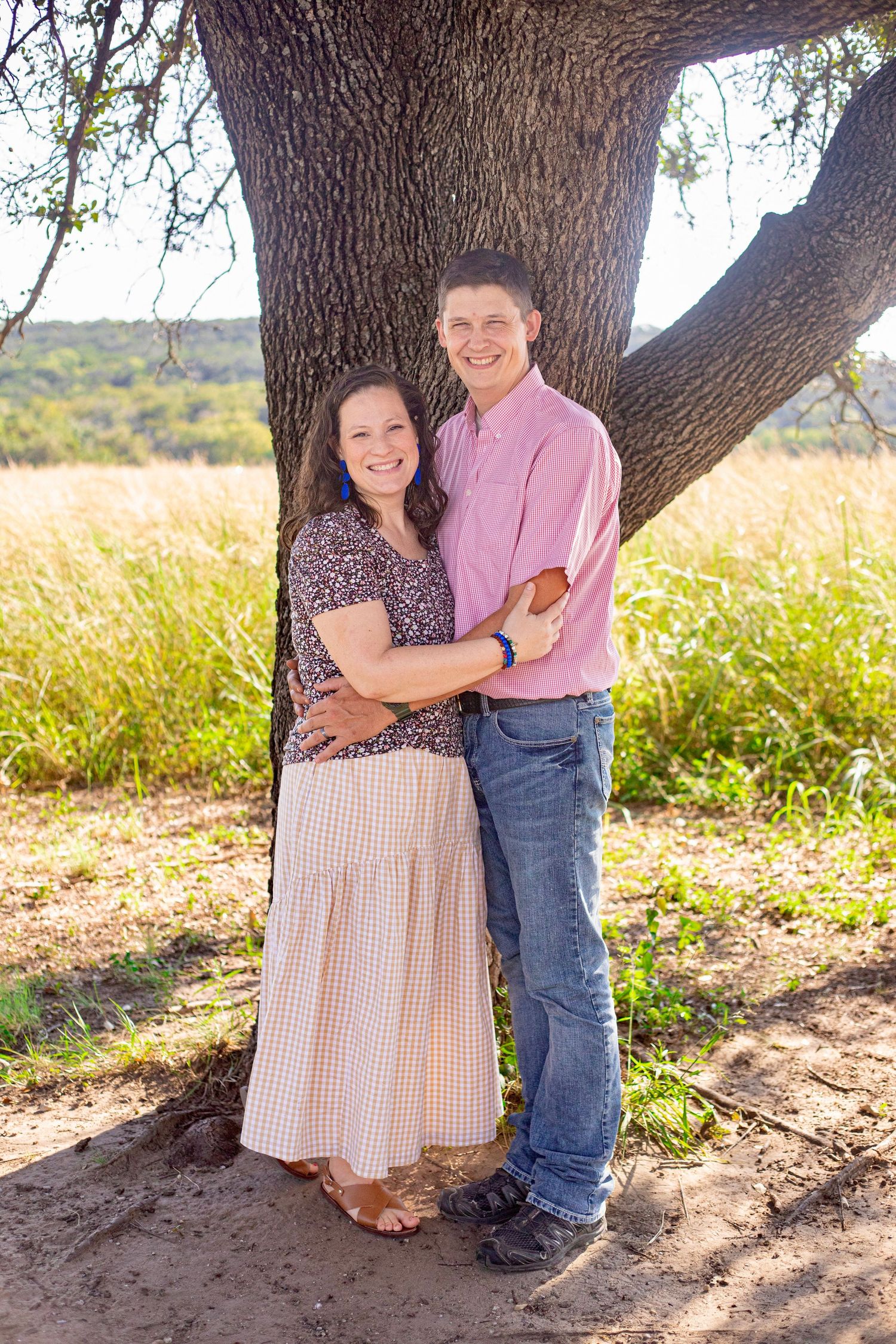 Two young children hugging by a tree trunk in a natural outdoor setting.