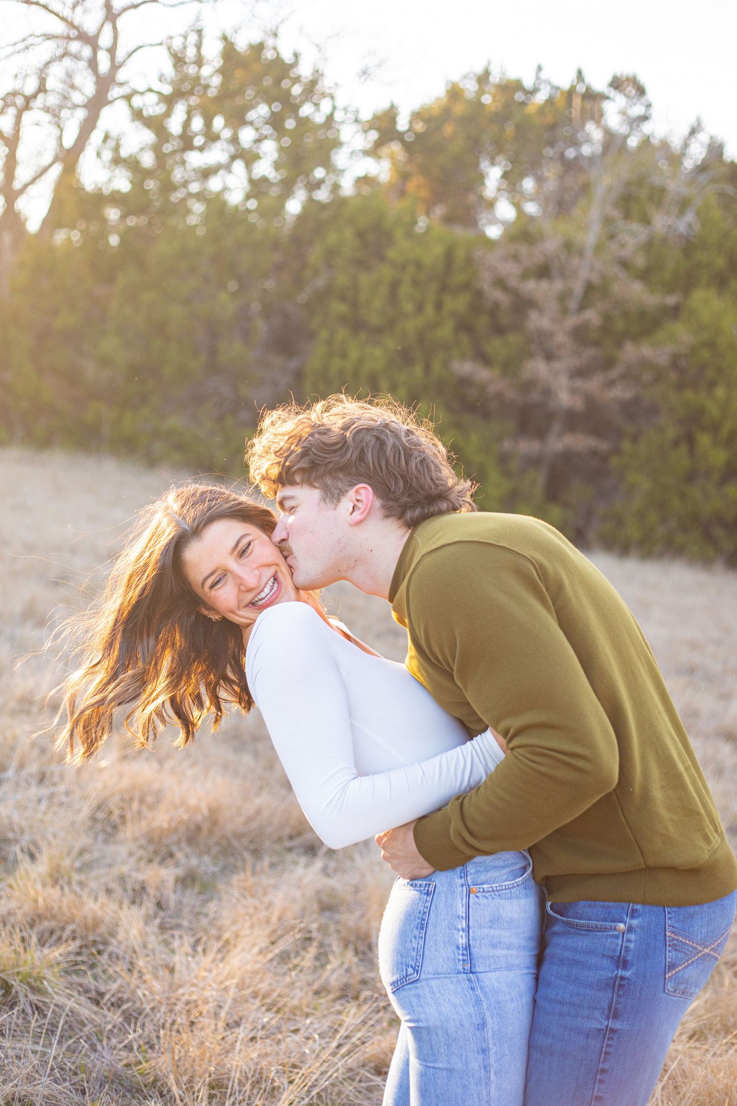 Couple laughing and embracing in a field during golden hour sunset.