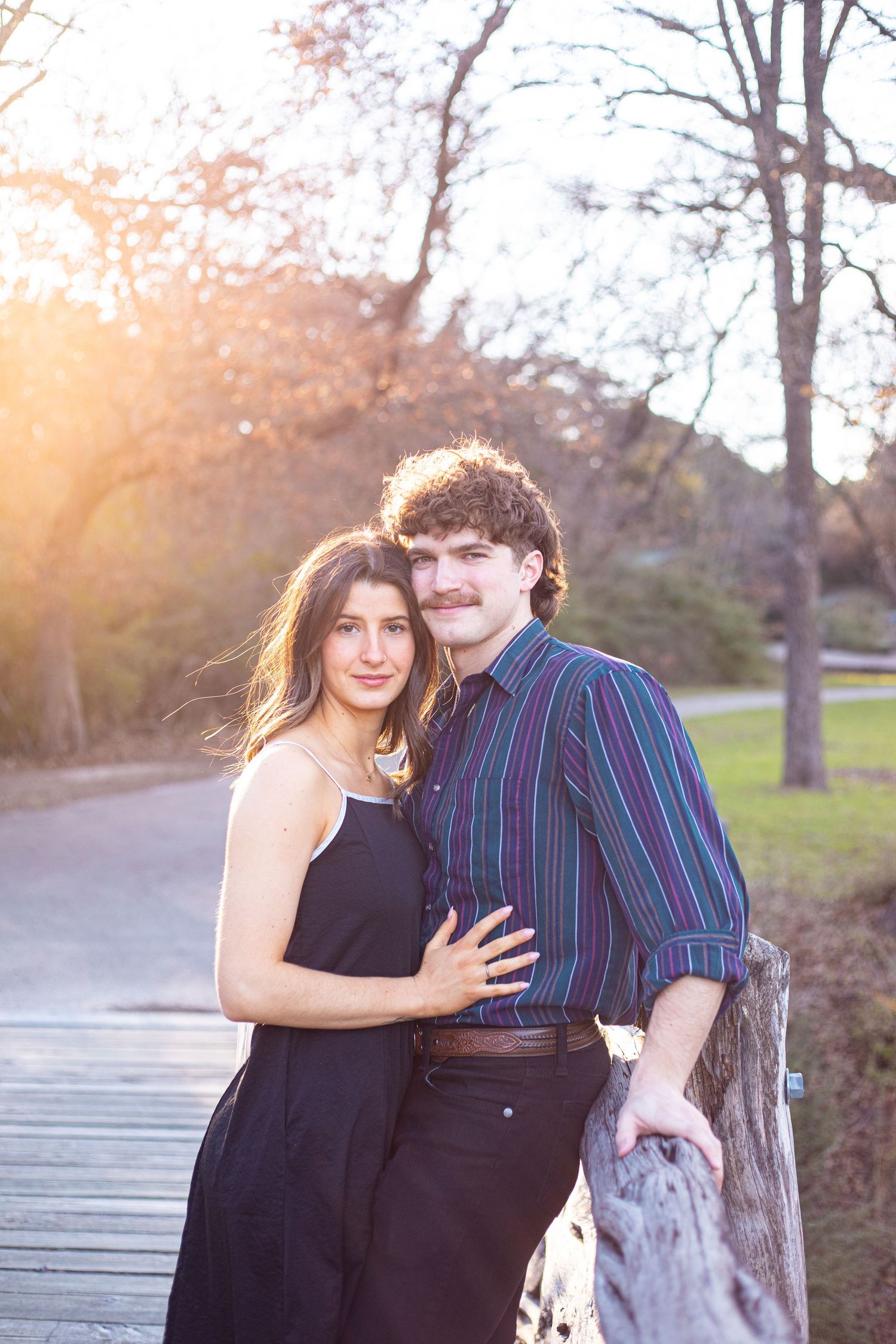 Romantic couple in casual attire posing together on wooden walkway at dusk.