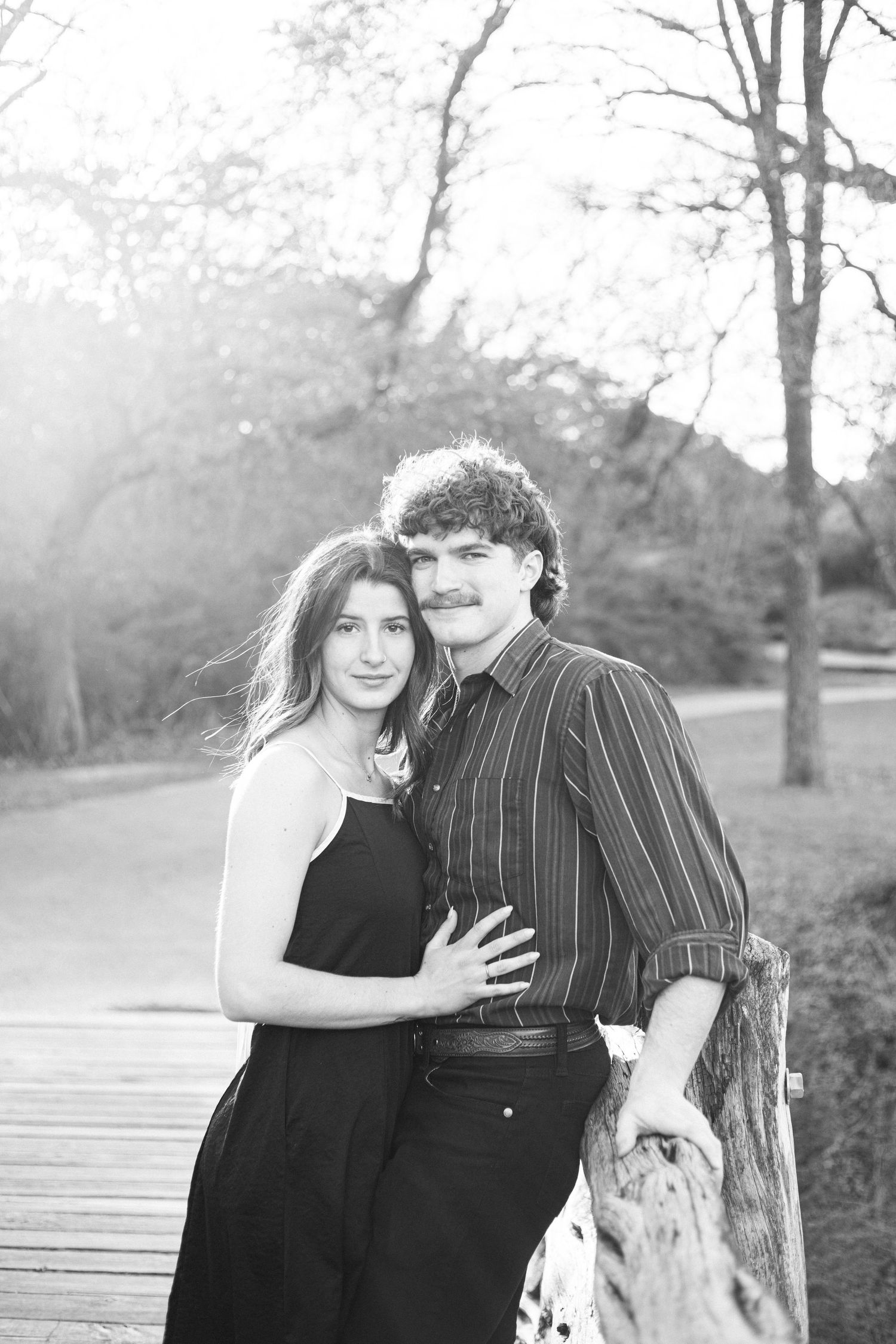 A couple poses together in black and white on a wooden boardwalk.