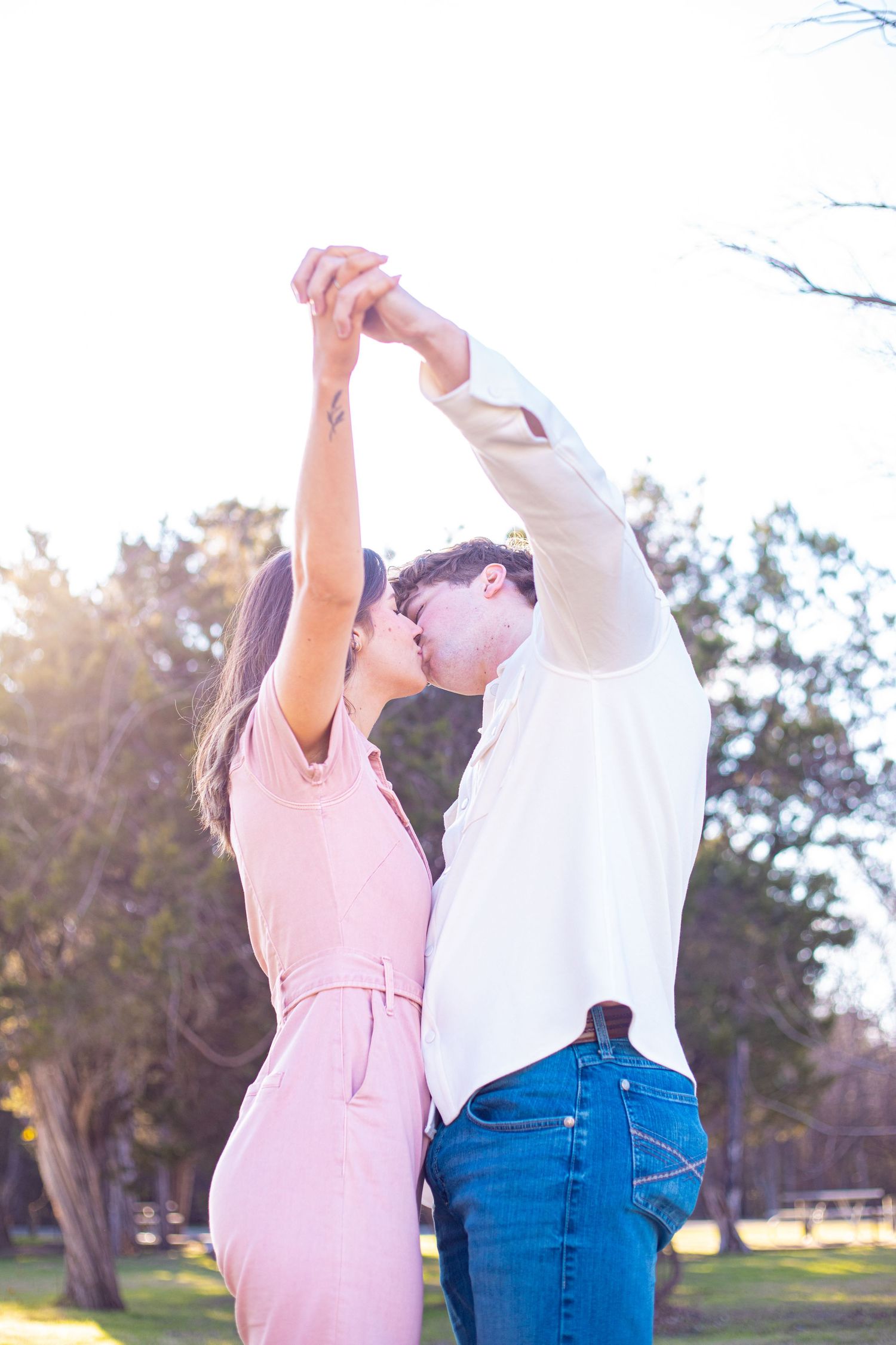 A couple in pink and white clothing dances together in a sunlit park.