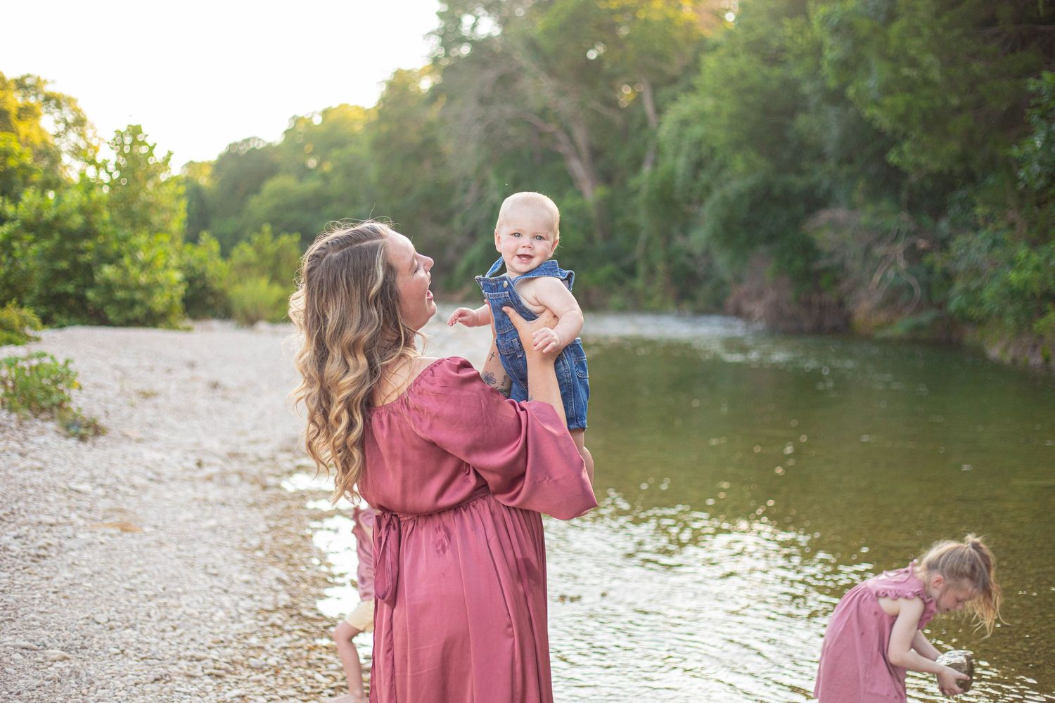 People in coordinating pink outfits explore a rocky riverbank surrounded by lush greenery.