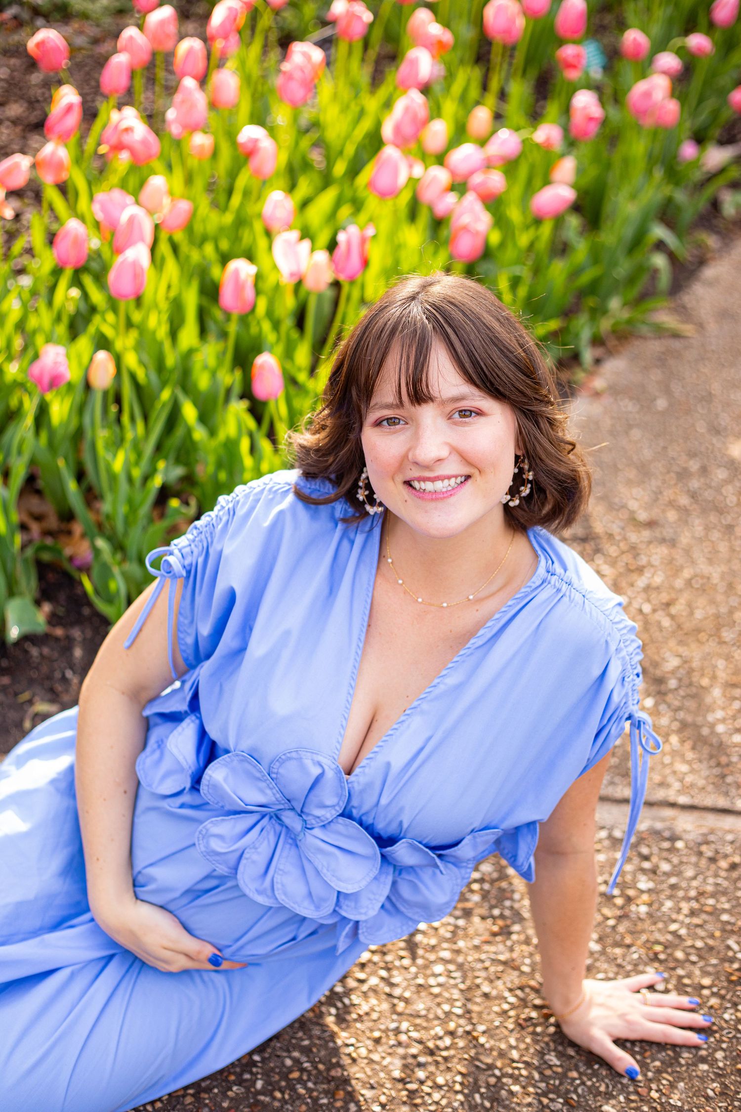 Woman in blue dress poses by pink tulips during spring garden maternity photoshoot.