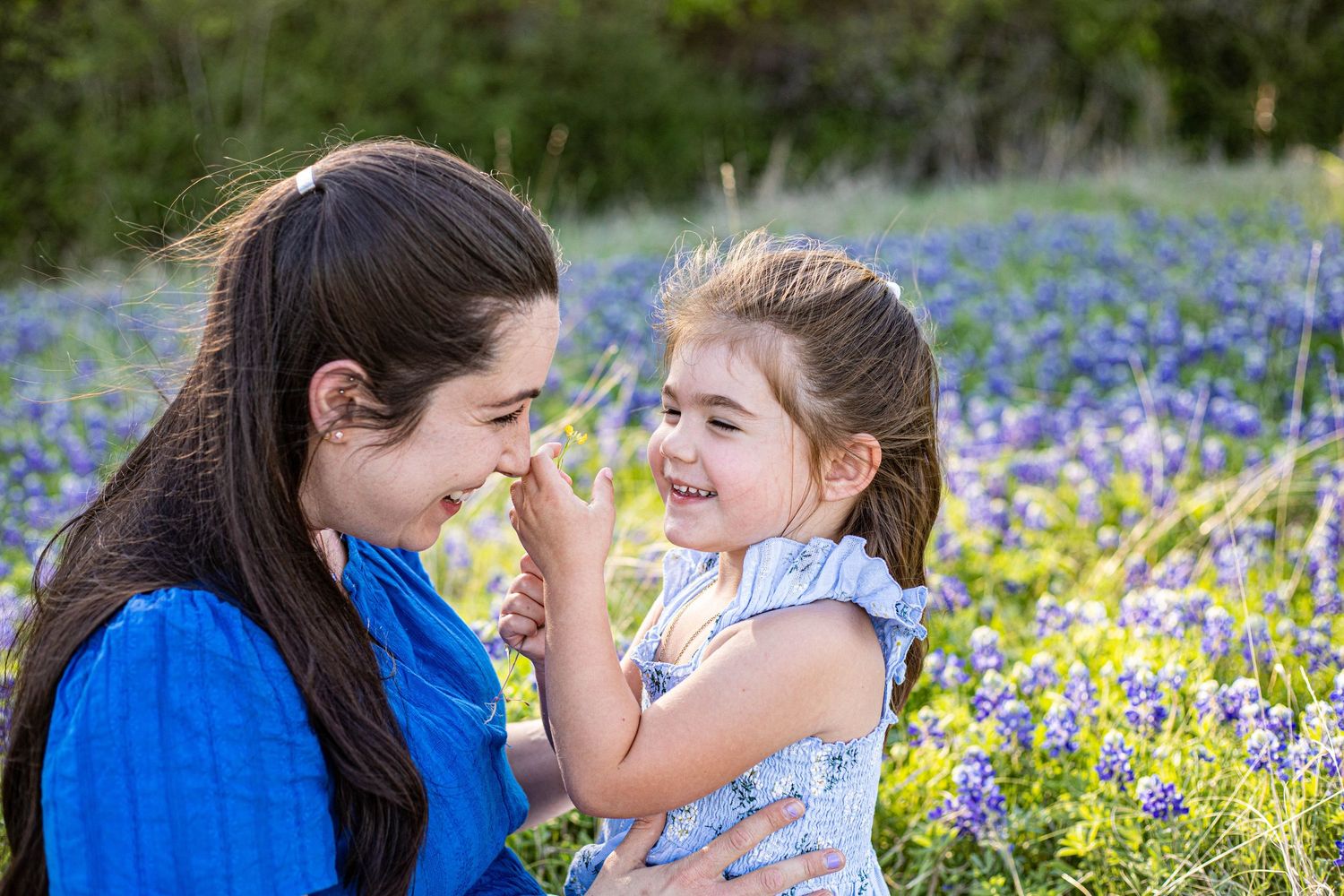 A mother and young daughter laugh together in a field of blooming bluebonnets in Texas.
