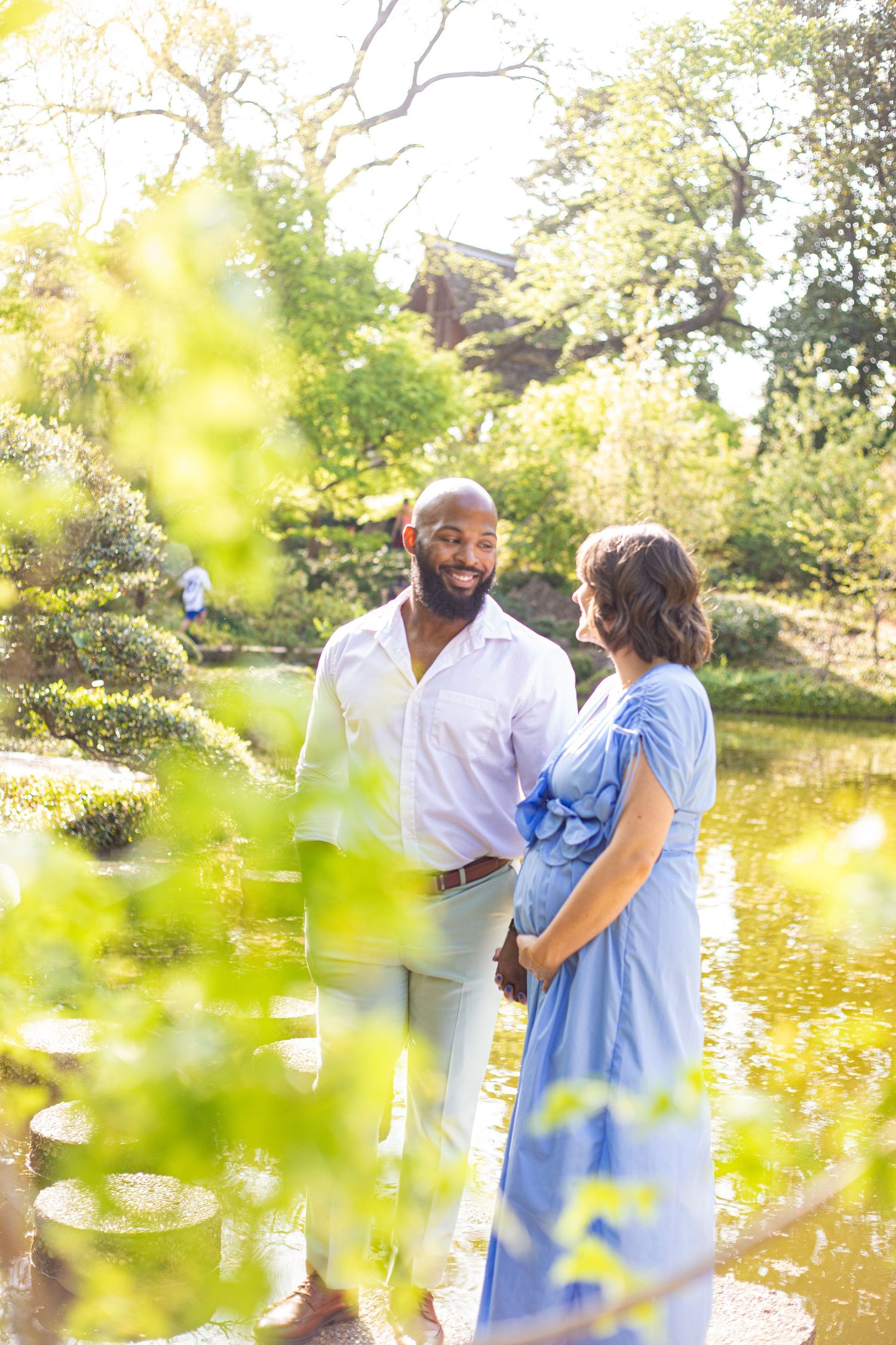 Couple sharing intimate moment by pond with golden sunlight filtering through trees.