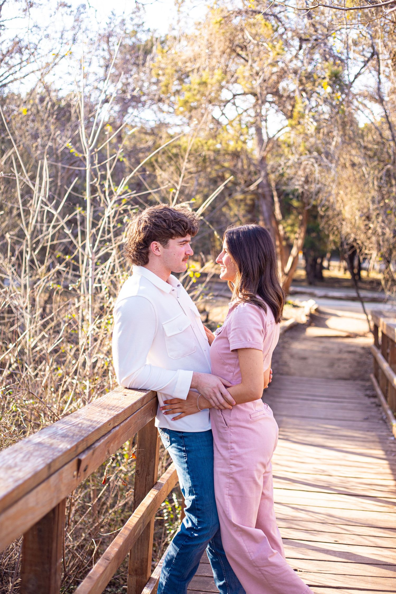 A couple shares romantic moments on a wooden boardwalk surrounded by nature.