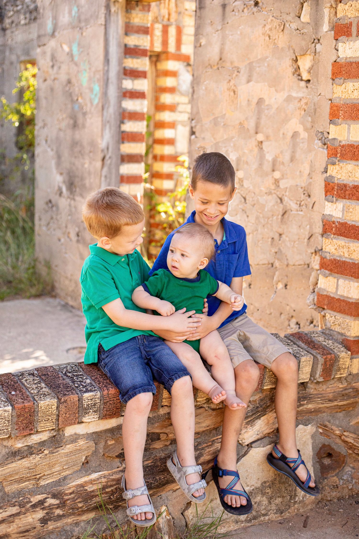 Three children sitting together on brick ledge sharing joyful moment against stone wall background.
