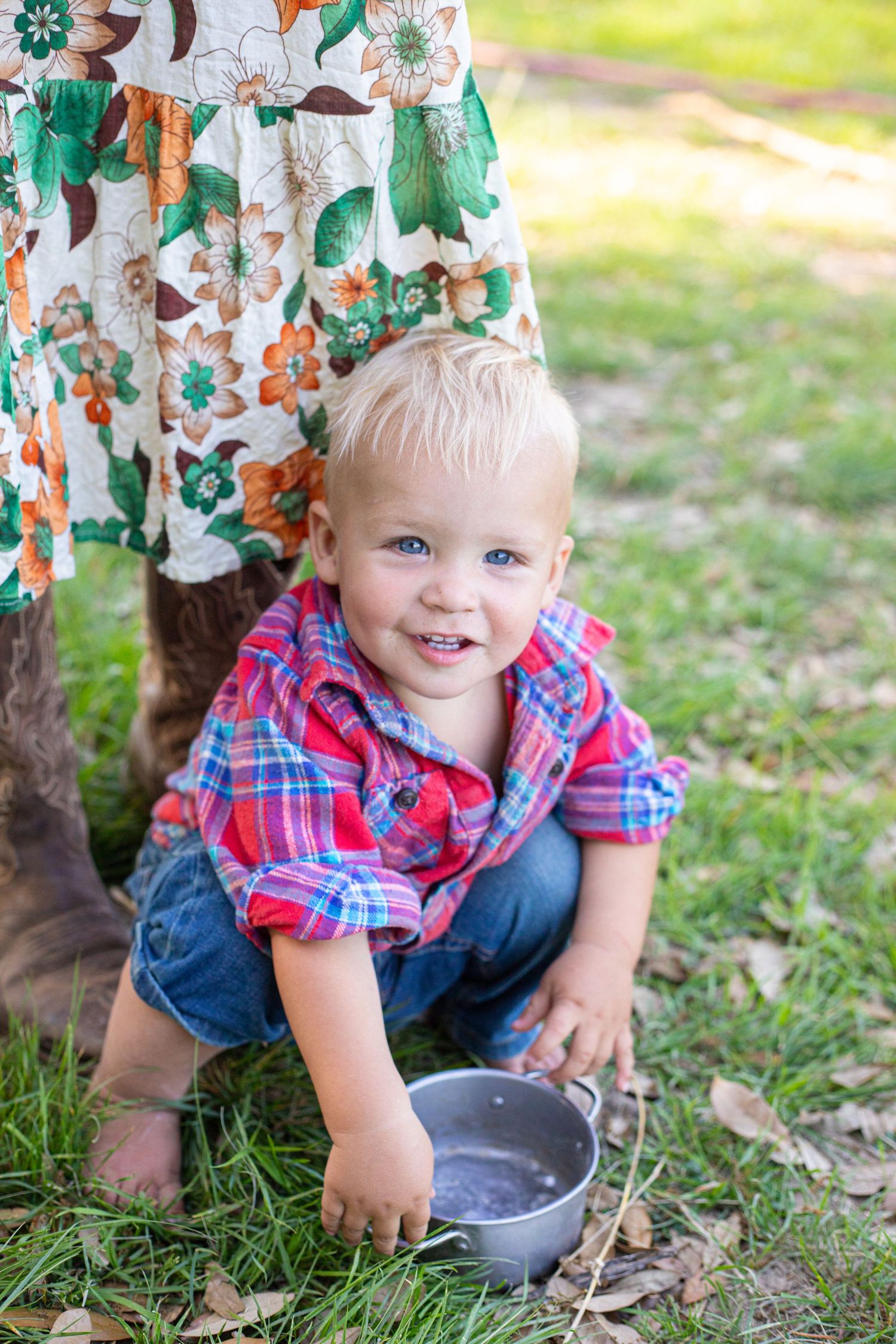 A small child plays in the grass wearing a red plaid shirt and denim.