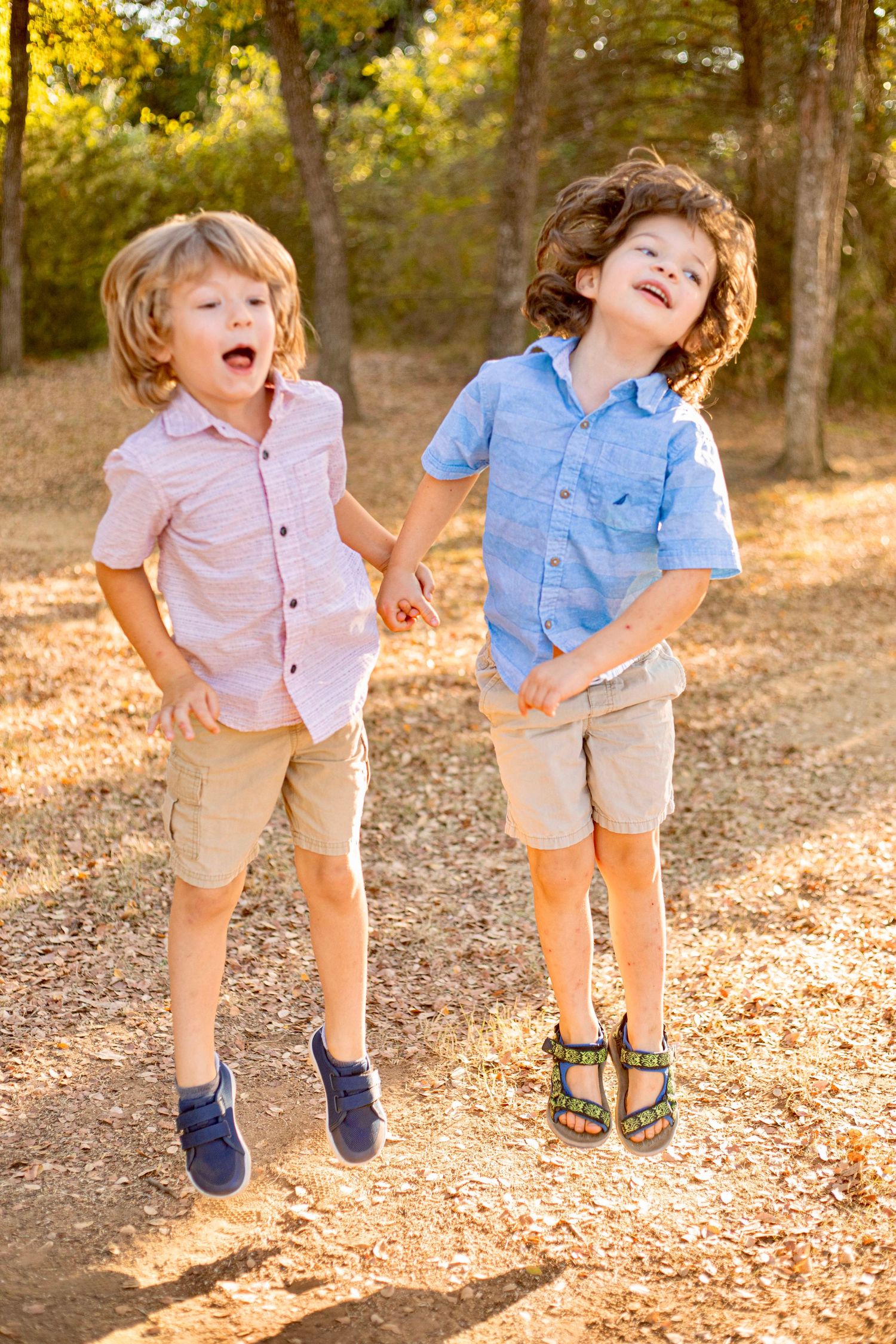 Two children jumping and laughing together on a sunlit forest path.