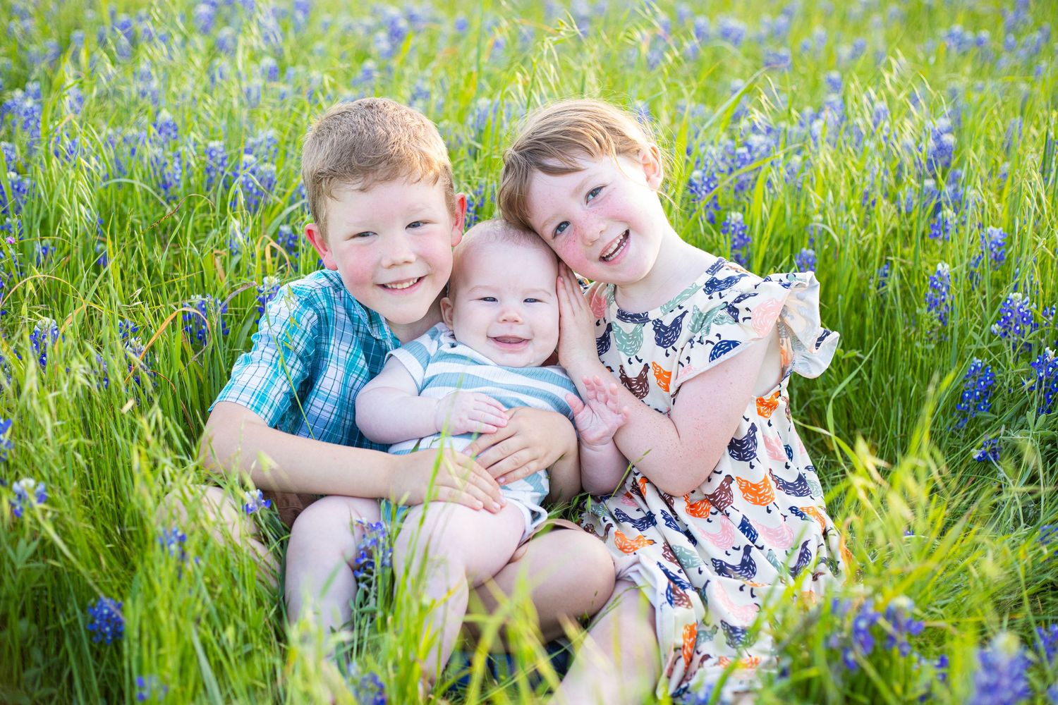 Children lying together in field of blue wildflowers on sunny day.