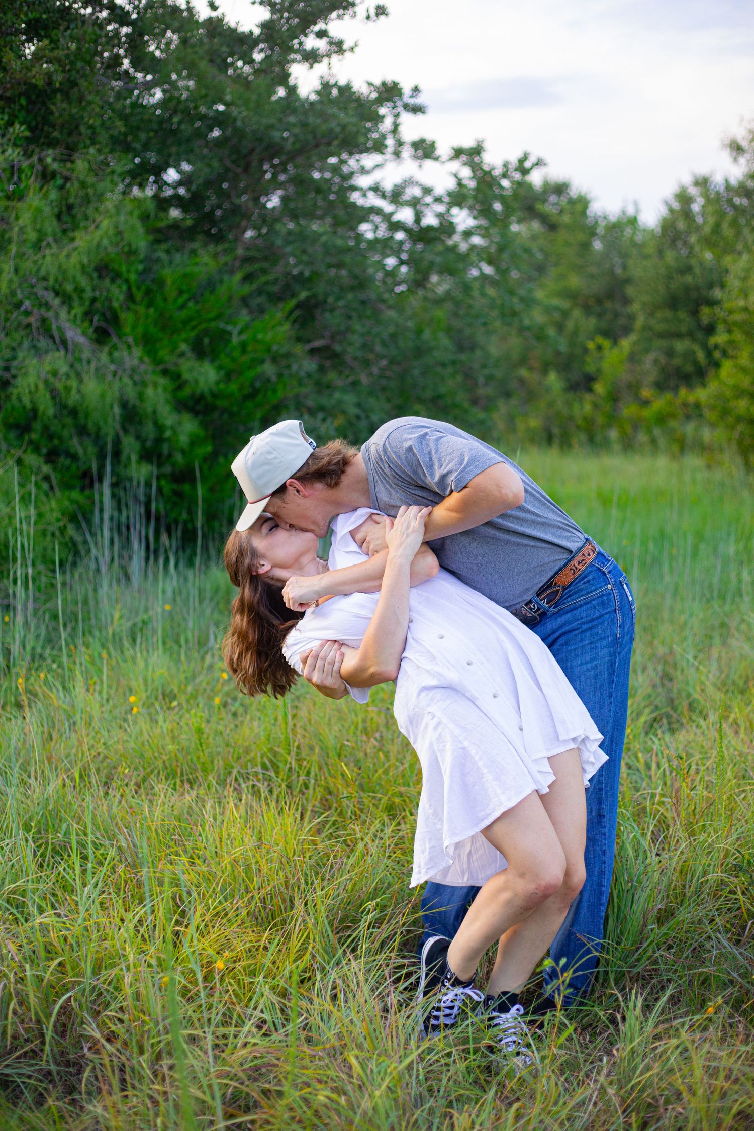 Playful couple in casual attire dancing in a grassy field.