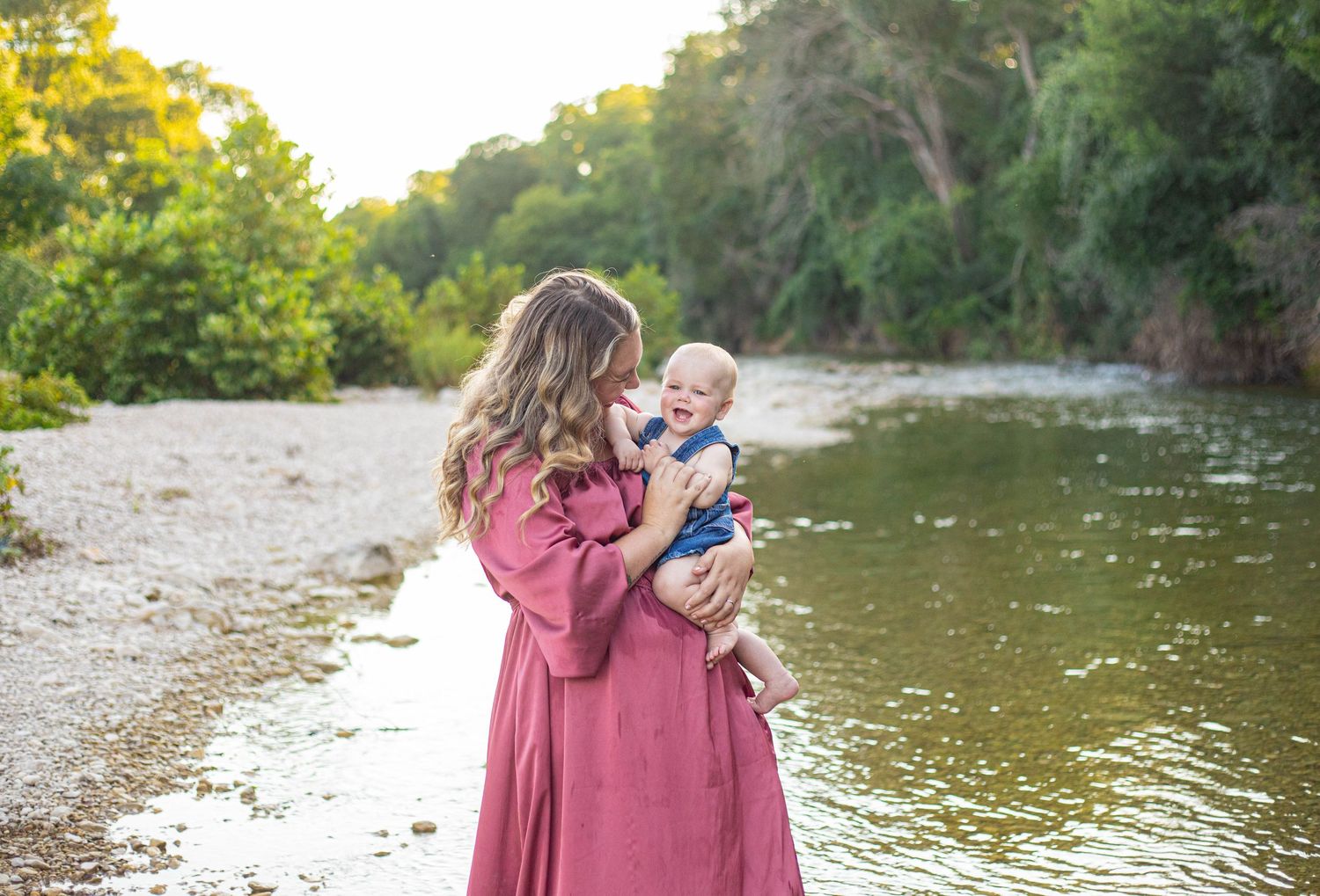 Family members share joyful moments along a sunlit river wearing pink and denim.