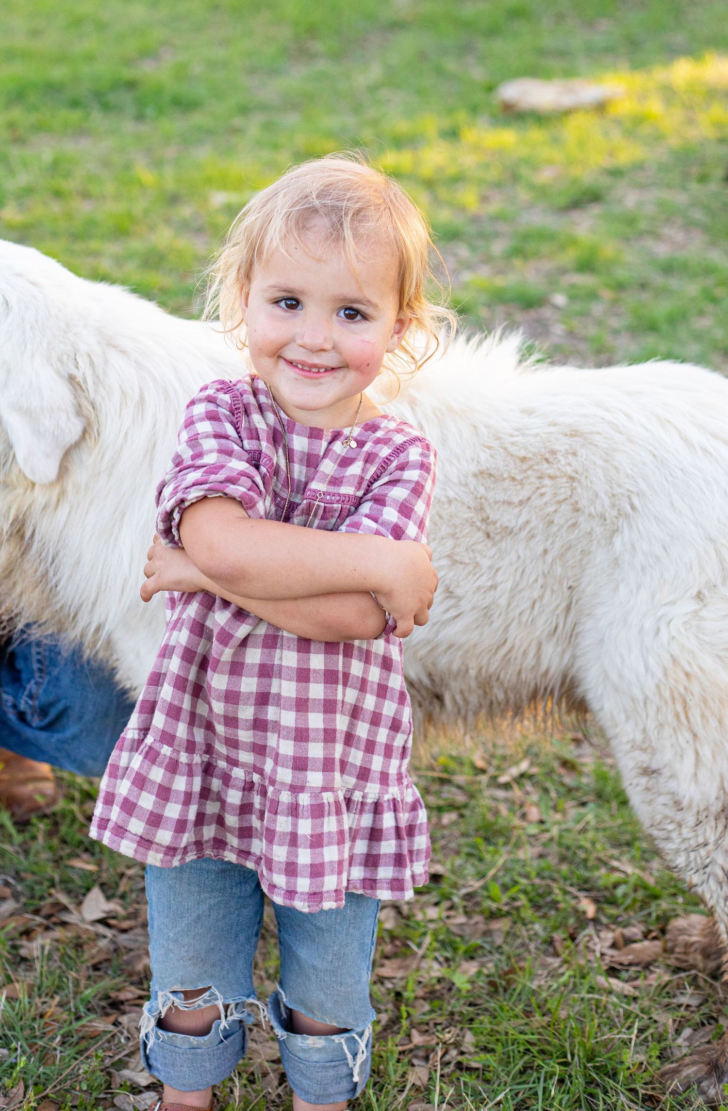 A child in plaid and denim poses near a white animal outdoors.