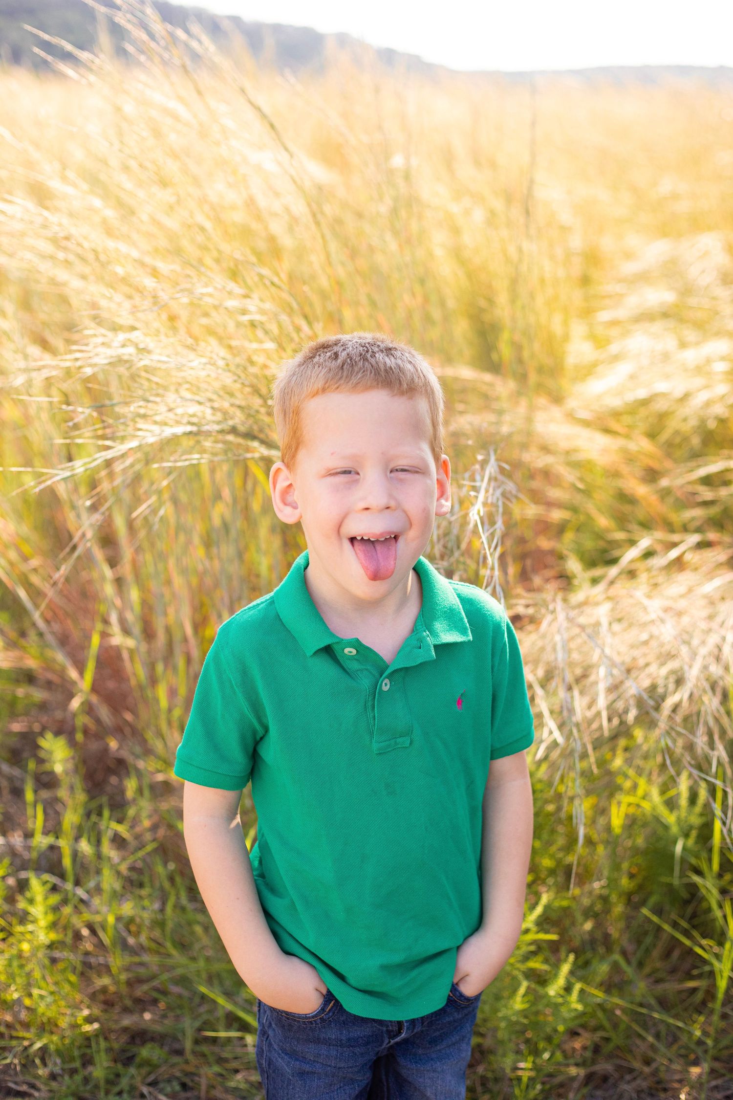 A child in a green polo shirt shows pure joy while playing in a wheat field.