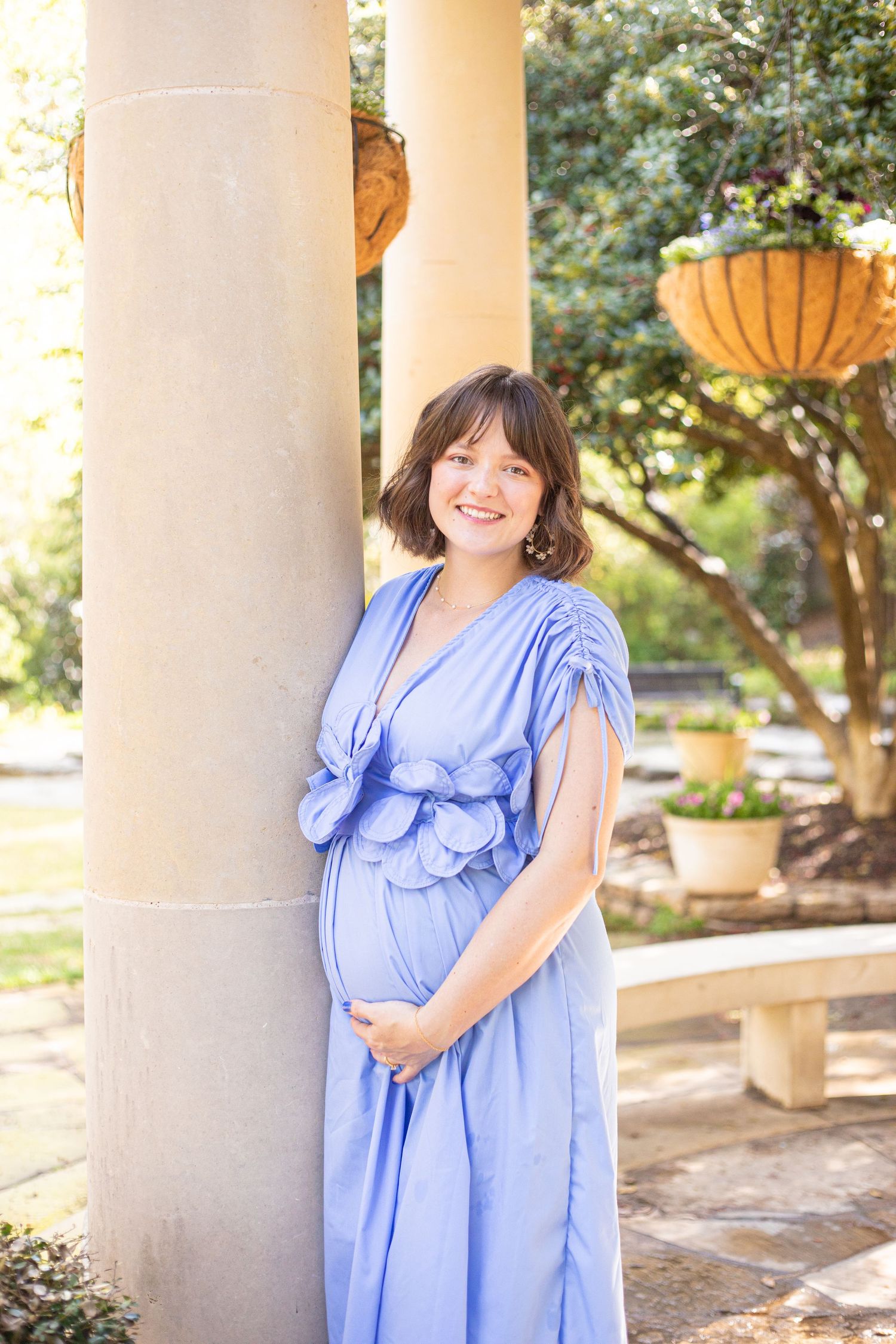 Person in light blue ruffled dress posing by white columns in garden setting.