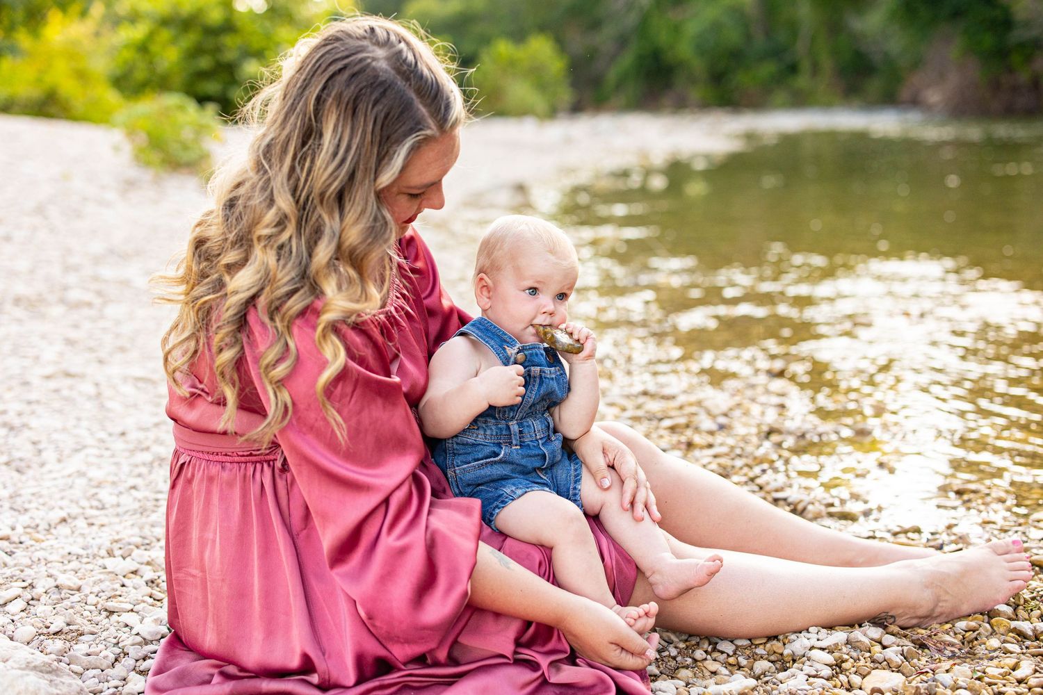 A tender moment captured by the water's edge with a pink dress and denim overalls against a natural backdrop.