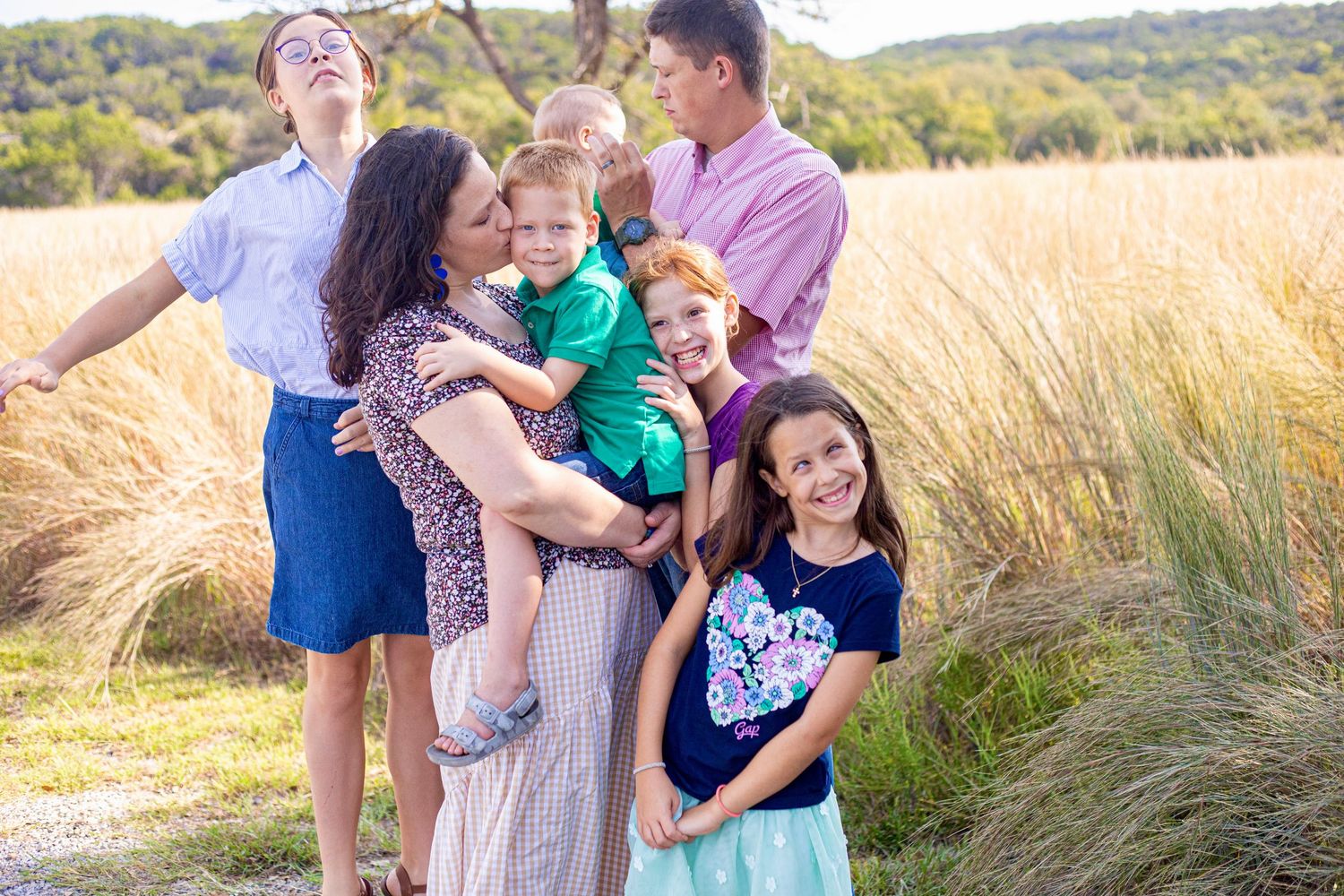 Happy family members embrace and laugh together in sunlit field.