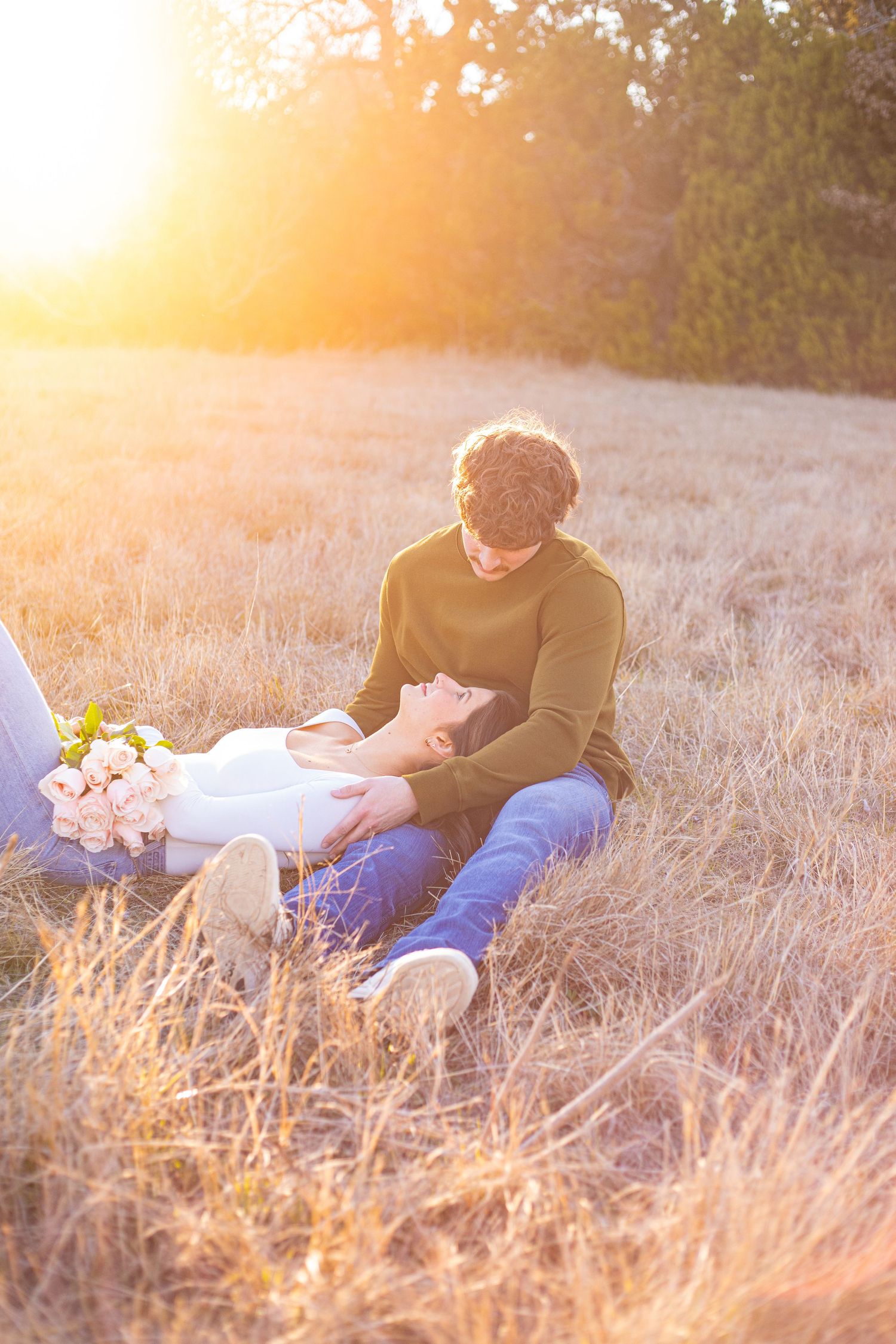 Couple relaxing in golden grass field during sunset with flowers nearby.