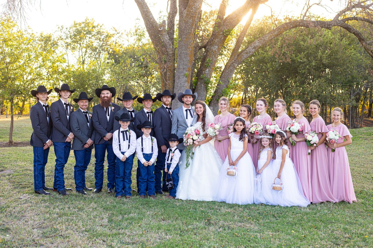 Wedding party in blue and pink attire poses outdoors during golden hour.