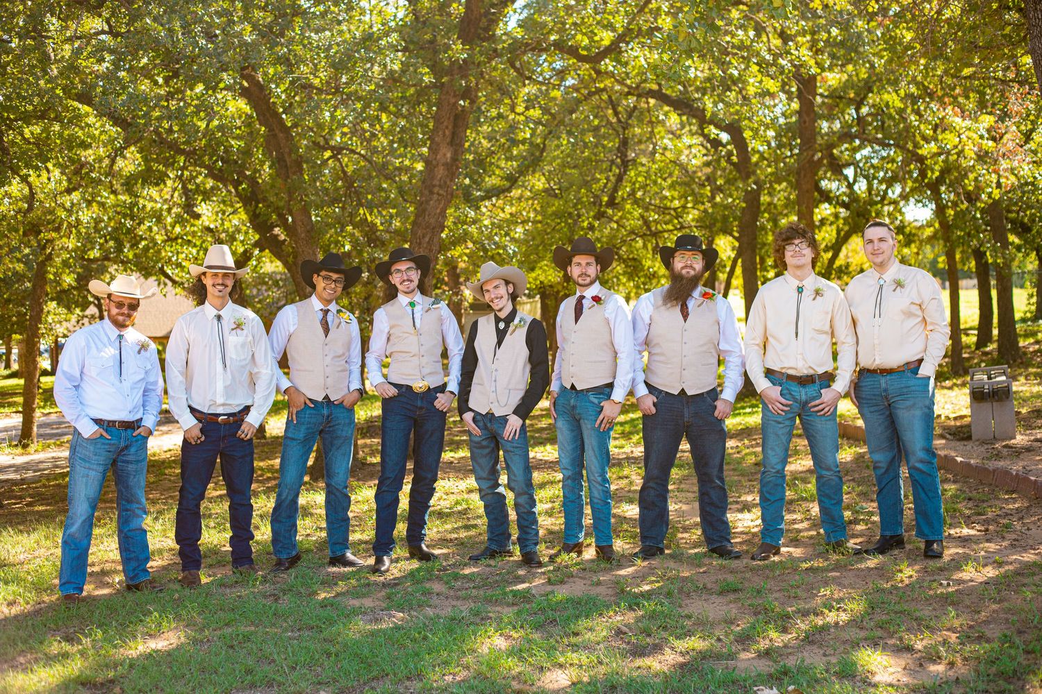 Groomsmen in casual attire with suspenders posing outdoors under trees.