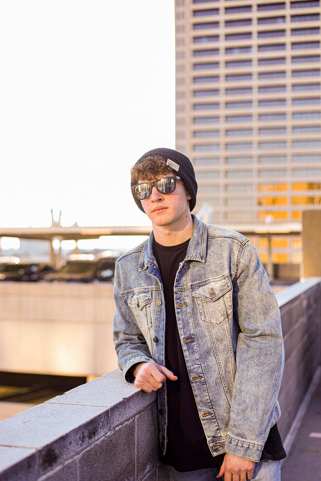 Urban fashion shoot featuring denim jacket and sunglasses against city building backdrop.