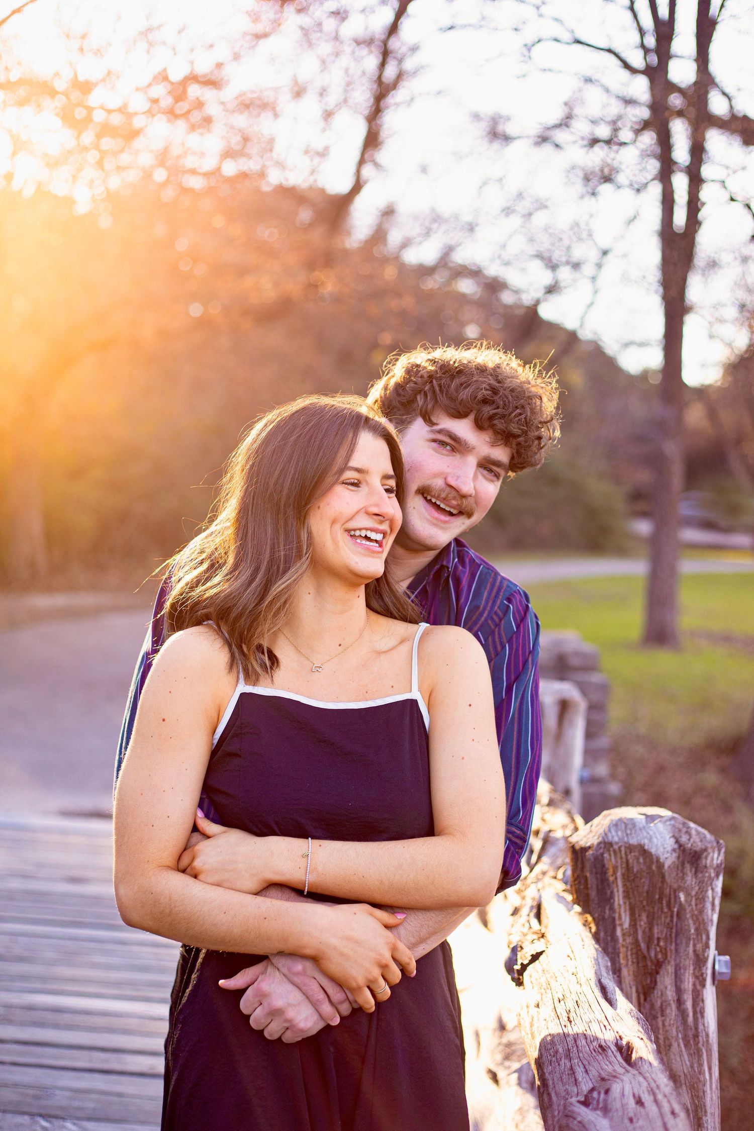 Romantic couple embraces during golden hour sunset photo session in a park setting.