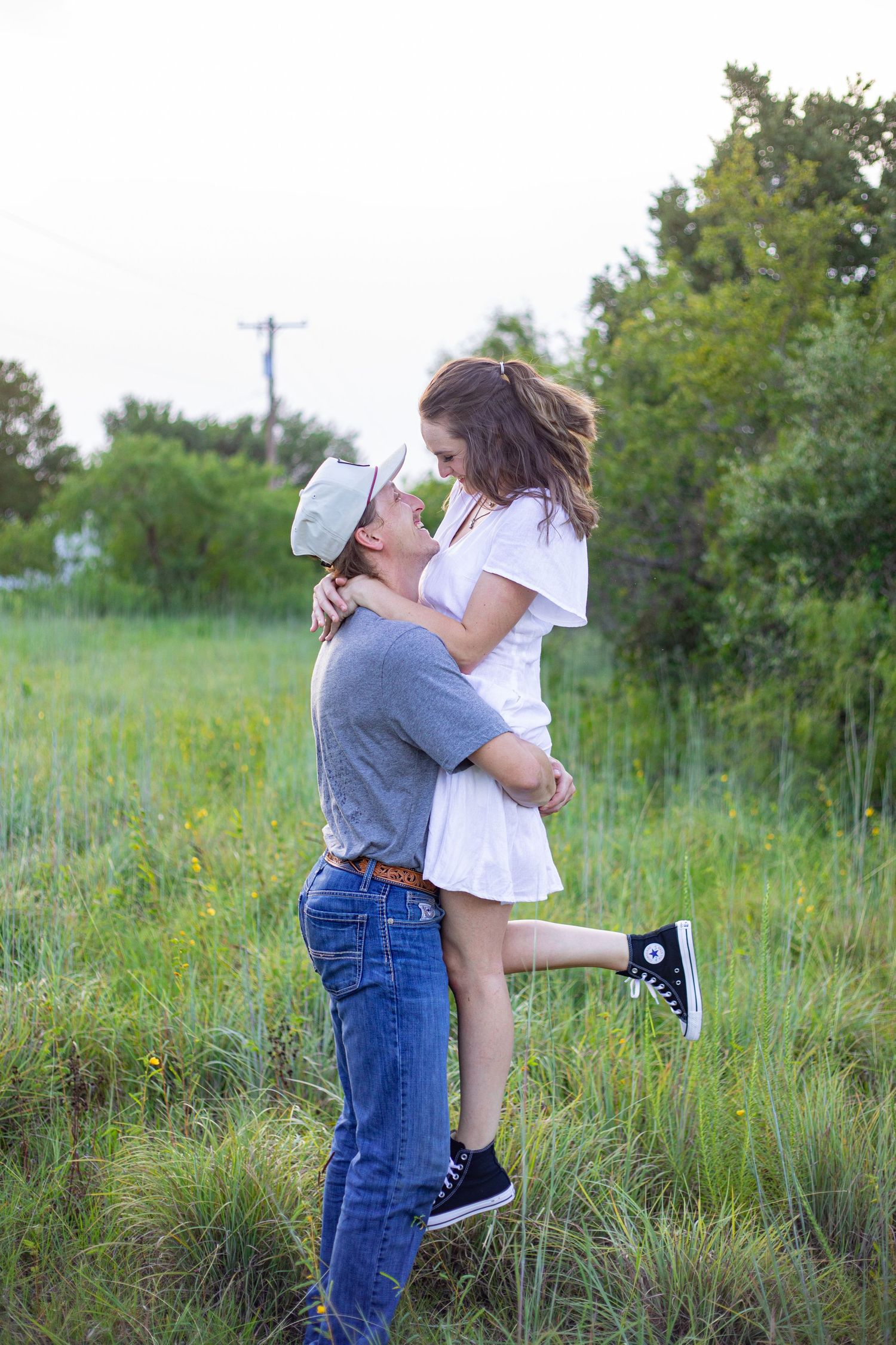 A couple embraces and lifts each other up in a grassy meadow during a romantic photoshoot.